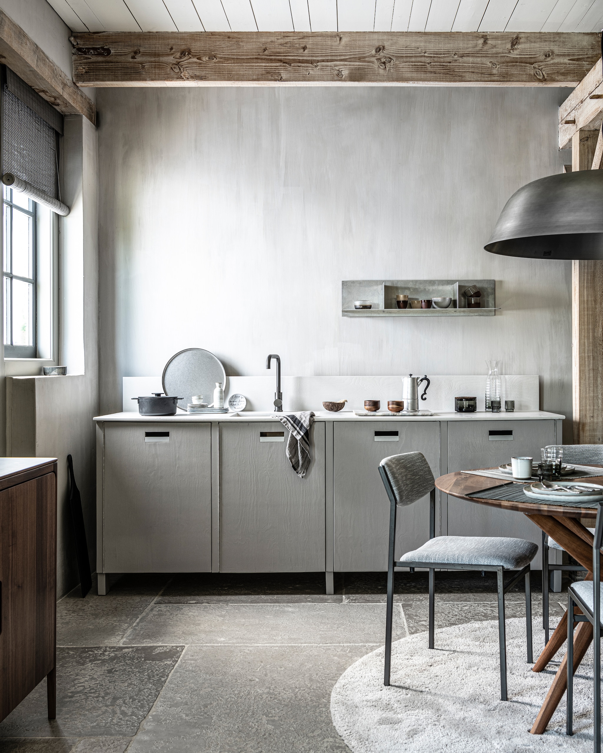 Keuken op maat gemaakt, prijs op aanvraag (com-anders.nl). Kraan gun metal € 169,- (tworooms.nl). Zwarte pan Surface van Serax € 126,-, glas Ripple van Ferm Living, set van 4 € 35,-, zwarte serveerplank Acacia van Bloomingville, 60x70 cm € 60,99, houten theekop Collage van Serax, per stuk € 12,80 (vtwonen.nl). Percolator Lady Anne € 59,-, tweekleurige keramieken mok Earth € 17,50, stonewashed rond stalen dienblad € 69,- (bymolle.com). Sake-set € 39,75 (japansewinkeltje.nl). Bord met geschreven tekst van Anouk Kramer € 30,- (archive-store.nl). Glazen opbergpot met houten deksel € 19,95, glazen karaf € 24,95 (nordal.eu). Wandplank Rivet, small, onbehandeld aluminium, 87,6x24,4x20,6 cm (bxdxh) € 615,- (framacph.com). Hanglamp Cloche Three, geborsteld aluminium, 81x25 cm (Øxh) € 750,- (vanduivenboden.nl). Vintage design stoel met nieuwe stoffering € 850,-, walnoothouten eettafel Lakri, 120 cm (Ø) € 2984,- (goeds.nl). Gehamerd bestek, per stuk € 5,99, bamboe placemat, set van 2 € 6,99 (zarahome.com). Ronde borden van HKliving vanaf € 11,95, rechthoekige borden van Serax vanaf € 11,95, mok van HKliving € 6,95, schaal € 10,95 (loftloft.nl). Walnoothouten dressoir Rikke € 2960,- (demachinekamer.nl). Rond grijs vloerkleed € 3034,- (homestede.nl). Roll-up gordijn bamboo flat sticks, prijs op aanvraag (nature-deco.com). Op de wanden kalkverf Warm Grey van Pure &amp; Original, 1 liter € 40,75 (pure-original.nl). vtwonen 11-2021 | styling Kim van Rossenberg | fotografie Sjoerd Eickmans