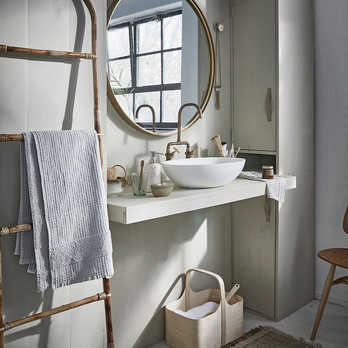 Grote ronde spiegel, marmeren zeeppomp (Nordal). Bamboe ladder, vloerkleed (Madam Stoltz). Witte wafeldoek (De Weldaad). Stoel Butterfly van Ercol (De Machinekamer). Berkenplex opbergmand (Nordic New). Grijze handdoek (Zara Home). Waskom Girona (Ton Scholten). Kraan (Jan van IJken Oude Bouwmaterialen). Tadelakt zandkleurig potje met deksel (MaisonNL). Bureaulamp (Vint. Amersfoort). Glas, linnen doek in opbergzak, witte opgerolde wafeldoek (De Weldaad). Zandkleurig met bruine kom, messing muurknop van Ferm Living, geurkaars in bruin glazen potje (Six and Sons). Rieten mand in kast vanaf (H&amp;M Home). Badborstel (Dille &amp; Kamille). De kast is geschilderd in de kleur Bone van Farrow &amp; Ball (De Ru). De muur is geschilderd in de kleuren Egg White en Light Grey van vtwonen (Karwei). beeld: vtwonen 05-2018 | fotografie Jeroen van der Spek | styling Cleo Scheulderman