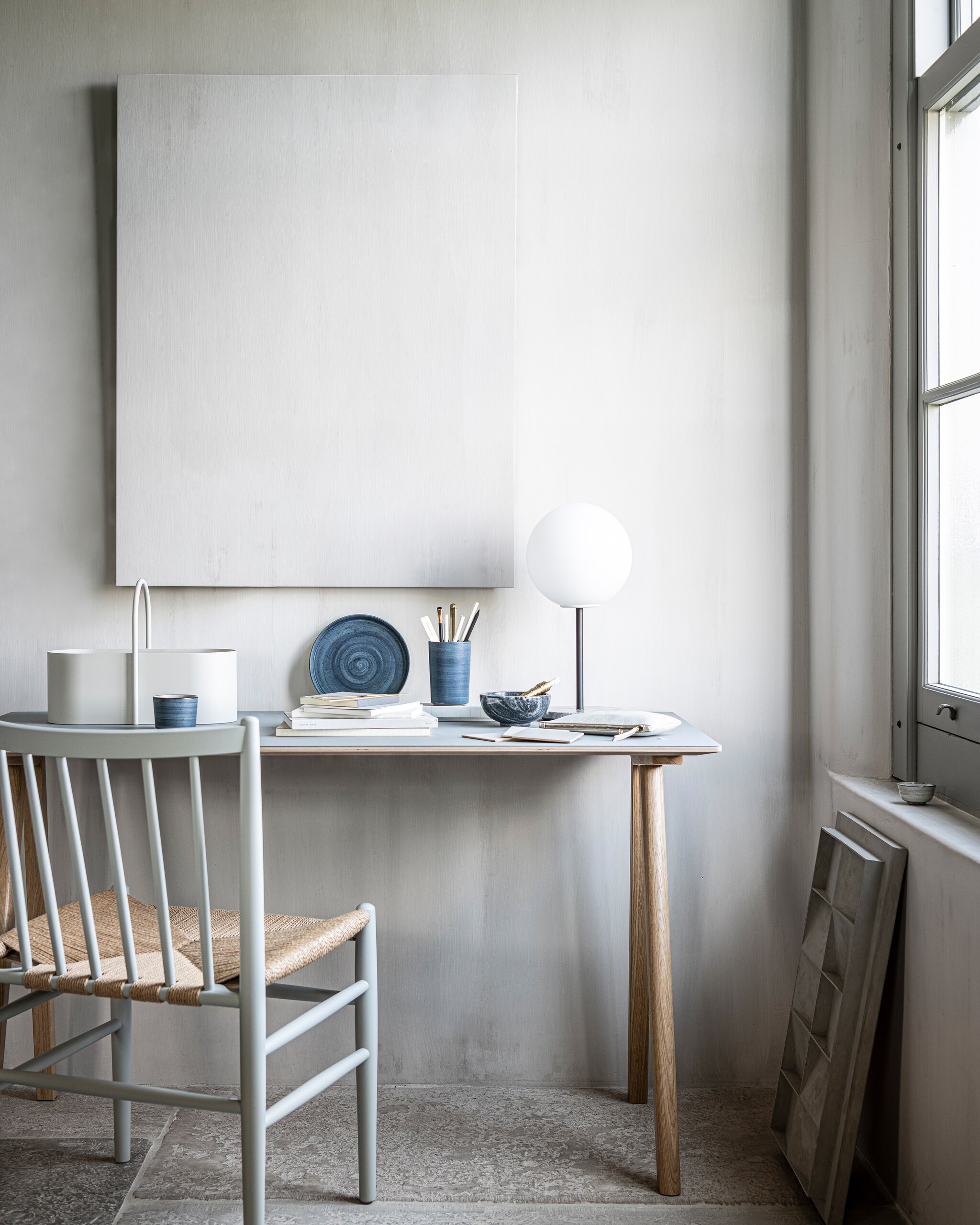 Op de wand kalkverf Old Flax van Pure &amp; Original 1 liter € 40,75 (pure-original.nl). Bureau CPH90 van Hay 130×65 cm € 699,-, tafellamp TR Bulb van Menu met grijs marmeren plateau, zwart metalen statief en opaal glas bol € 158,99, grijze toolbox Grib van Ferm Living € 65,- (vtwonen.nl). Kunstwerk N°05 in kleur Stone, 60×40 cm prijs op aanvraag (atelierledition.com). Blauw servies vanaf € 88,95, houten stoel met gevlochten zitting FDB Møbler vanaf € 649,- (letoile.store). Overig privébezit. vtwonen 11-2021 | Styling Kim van Rossenberg | Fotografie Sjoerd Eickmans | Assistentie Sanne van der Beek en Meike Linthorst