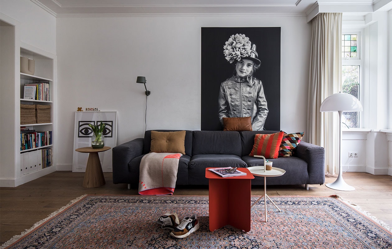 Print links: Ögon Cacao van de Zweedse grafisch ontwerper Olle Eksell. Bijzettafel Kwantum. Vaas Muuto. Wandlamp Tonone Bolt. Bank gekocht tijdens een garagesale. Plaid op bank Adelheid Laden. Kussens: bruin Hay, cognac Leen Bakker, gestreept Hay, wybers Ikea. Print achter bank foto van dochter Meis gemaakt door Maaike en geprint op Gekkotex, een zelfklevend polyester. Vloerkleed kringloop. Sneakers Atlantic Stars. Rode bijzettafel Puik Hinge. Witte bijzettafel Hay. Mok HKliving. Vloer van Amerikaans eiken lag er al. Muurverf wit RAL 9016 van Sikkens. vtwonen 10-2021 | Productie en Fotografie Corine Hoge Bavel