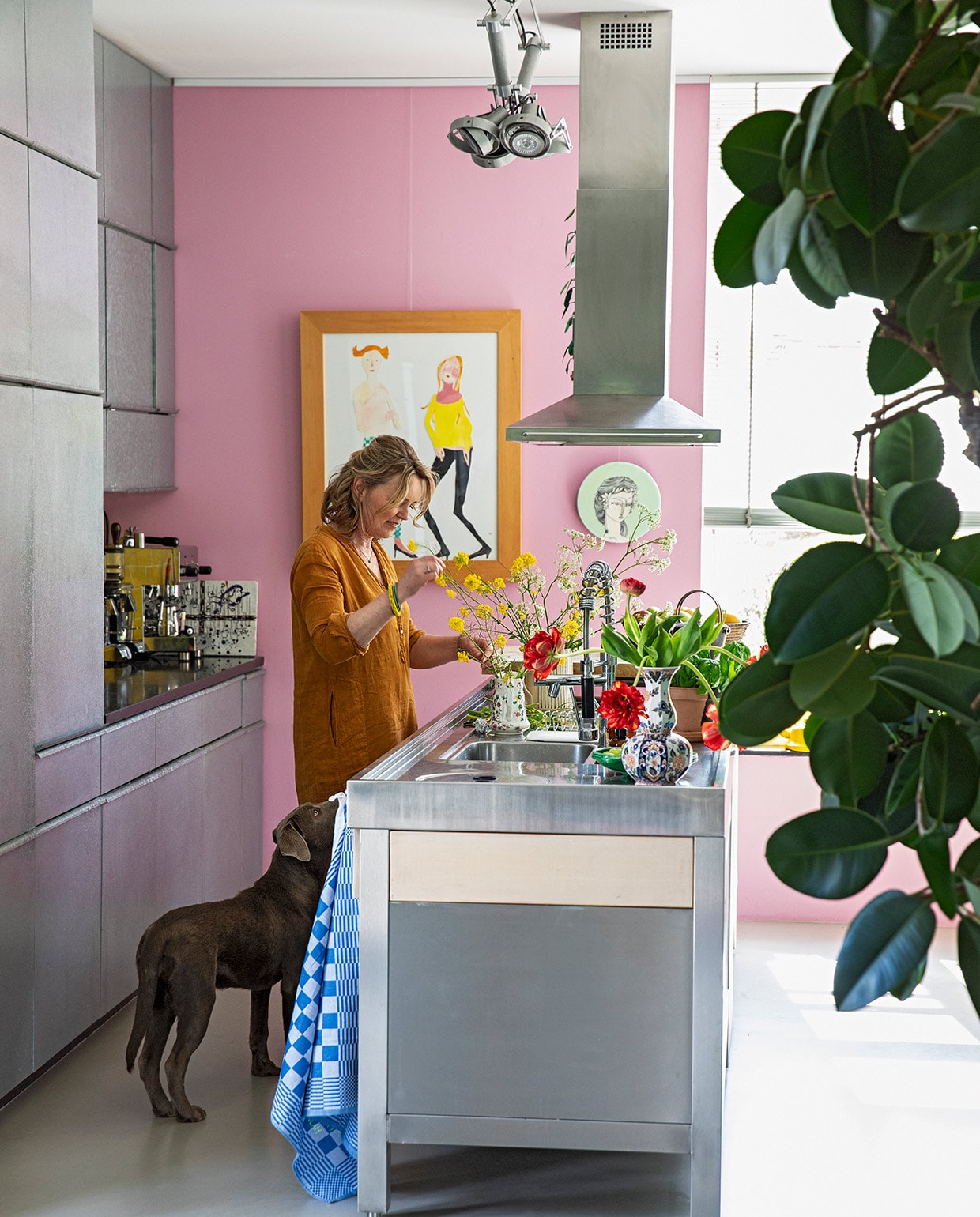 Karen aan het kookeiland van rvs en eikenhout. Apparatuur Smeg. Op maat gemaakte keuken met fronten van zink. Lamp Modular. Kunst Vanessa Beecroft. Wandbord meegenomen uit Australië. Roze muurverf Histor S0540-R30B. Overig herkomst onbekend. vtwonen 07-2021 | styling Ilona Jongepier | fotografie Dana van Leeuwen