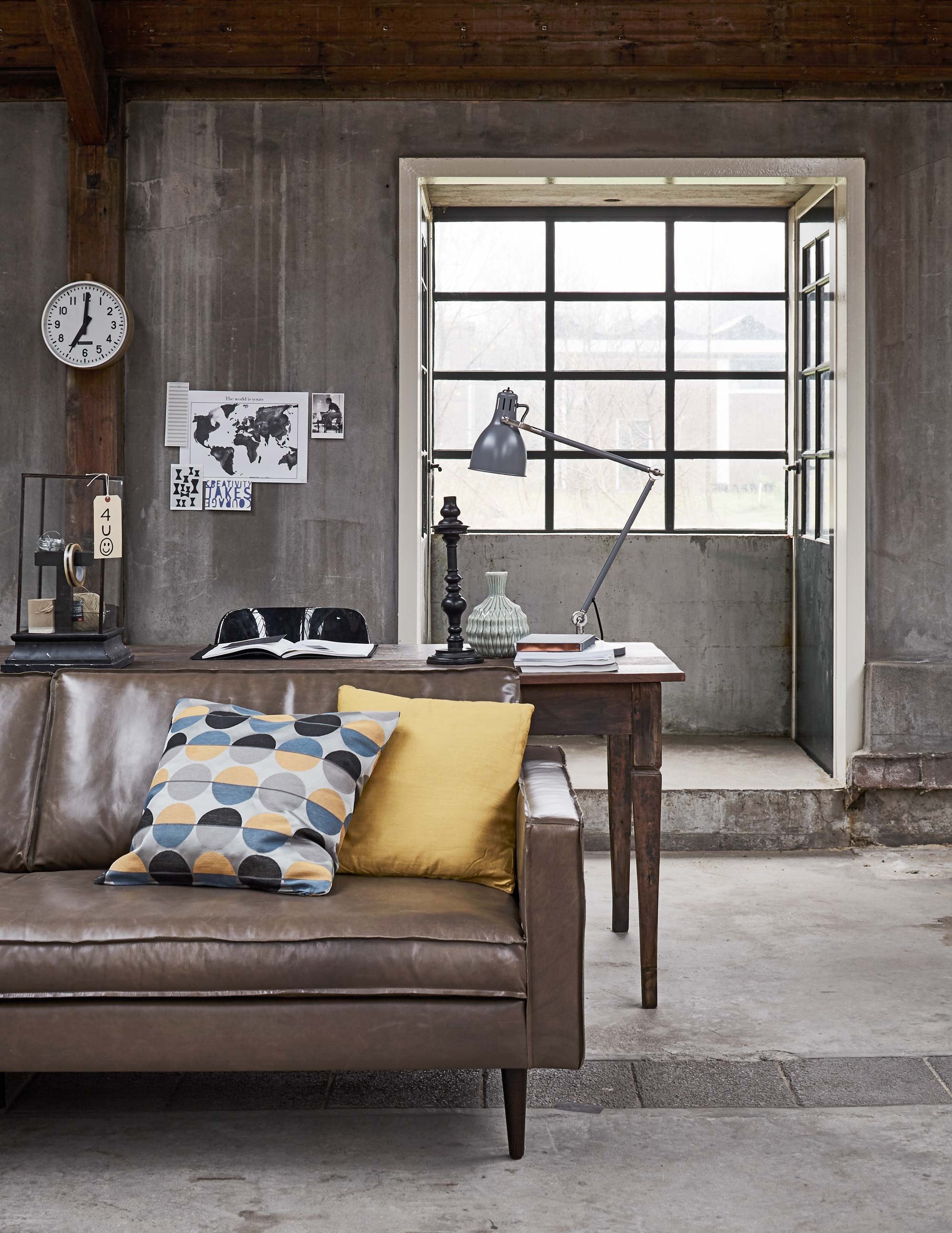 Oude teakhouten tafel (Jan van IJken Oude Bouwmaterialen). Bank Slimm in leer, kleur Fango (Design Loods 5). Zwarte Revolt stoel, klok, letter T in vitrinekast (Neef Louis). Vierkante stolp, kandelaar (De Weldaad). Groenige vaas (HK Living). Overig privébezit.