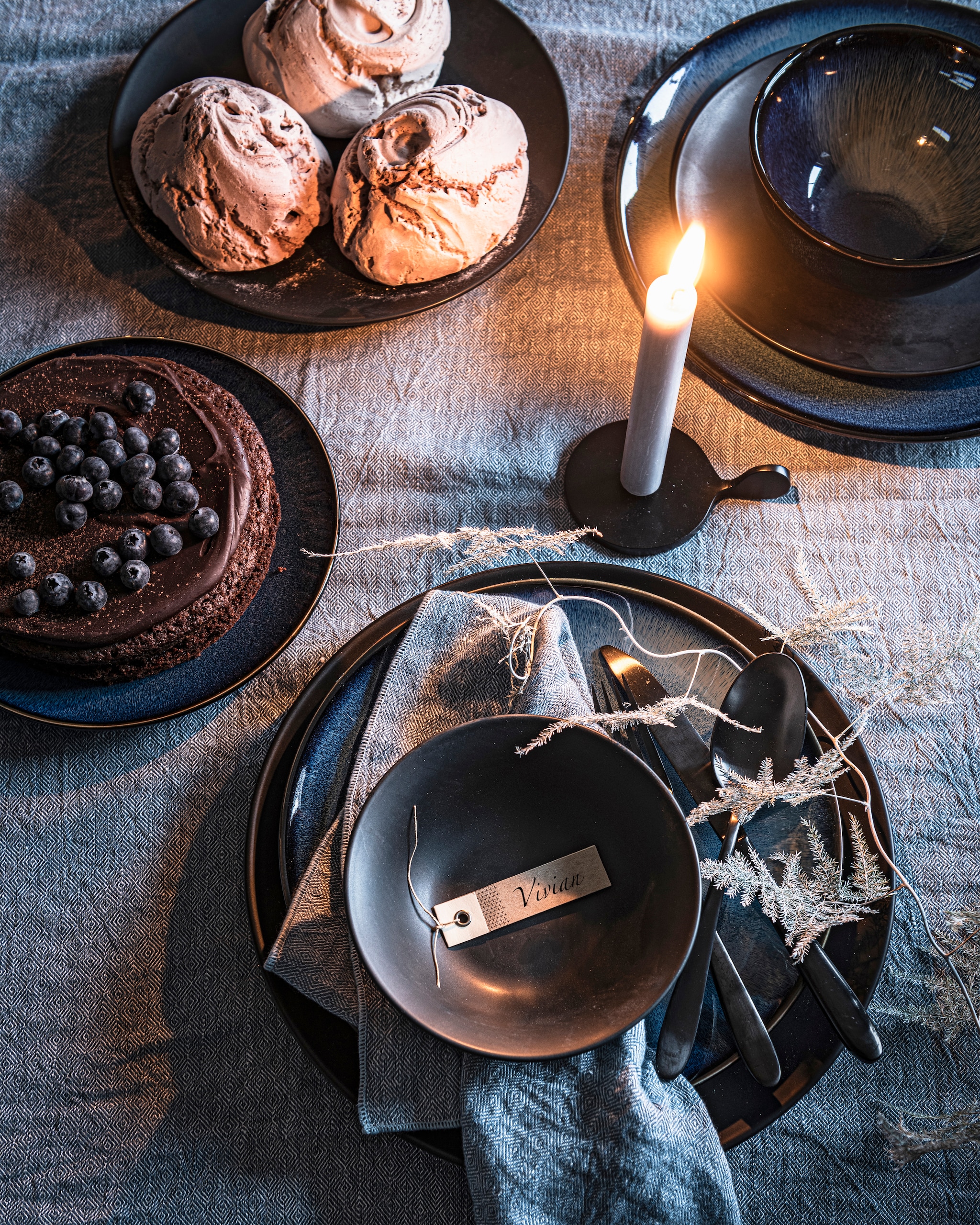 Donkerblauw porseleinen servies, 16-delig € 99,-, ook verkrijgbaar als losse onderdelen vanaf € 3,95. Matblauw porseleinen servies, 16-delig € 99,- of 36-delig € 239,-, ook verkrijgbaar als losse onderdelen vanaf € 4,50. Matzwart porseleinen servies 16-delig € 99,- of 36-delig € 239,-, ook verkrijgbaar als losse onderdelen vanaf € 1,95. Diverse metalen kandelaars zwart en donkerblauw vanaf € 8,95. Glazen vaas 22×31 cm (Øxh) € 69,95. Linnen tafelkleed, 150×250 cm (bxl) € 79,95. Zwarte ornamenten ring 100 cm (Ø) € 24,95 (ook in formaat 80 cm (Ø) € 19,95 en in kleur ijsblauw).M.m.v. com-anders.nl (kast en tafel), sostrenegrene.com/nl (stoelen met stof). Overig privébezit.Spread 1 beeld rechts (bovenaanzicht servies) vtwonen 12-2021 | Styling Kim van Rossenberg | Fotografie  Sjoerd Eickmans | Productie Tanja Saarberg