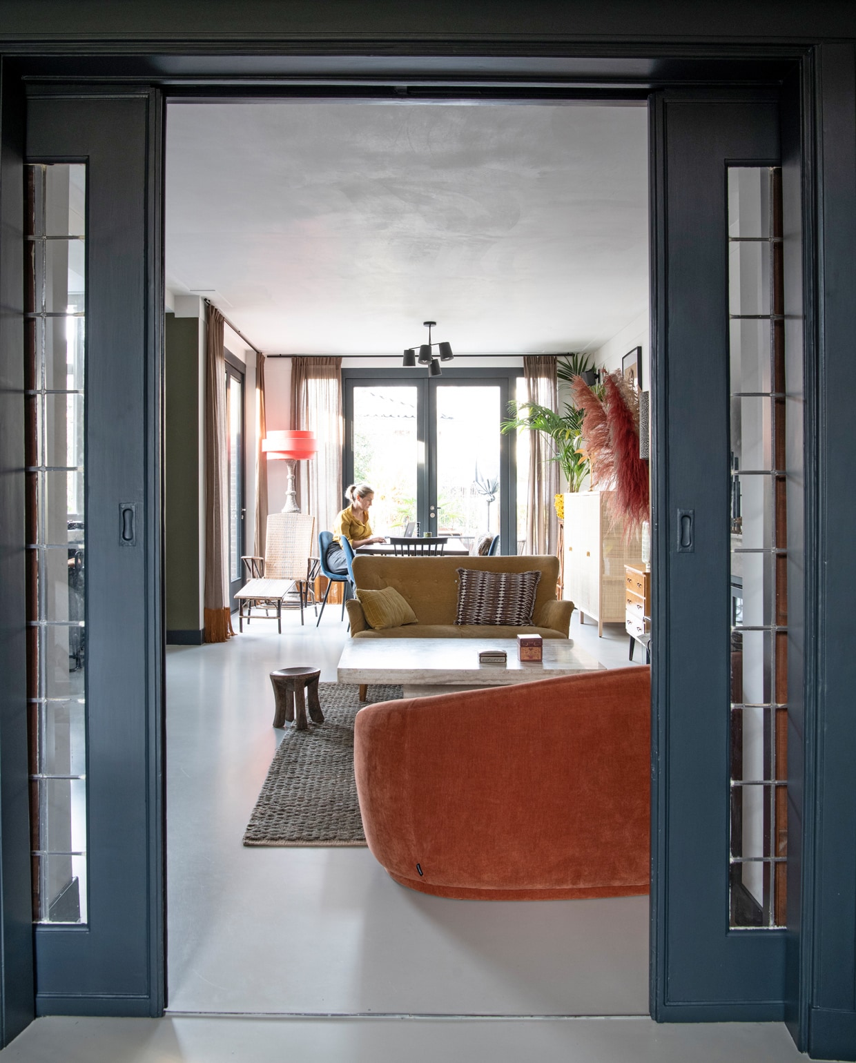 Blauwe verf op deuren Railings van Farrow &amp; Ball. Juten vloerkleed Crowd in Forest Green van Brinker Carpets. Kruk souvenir uit Tanzania. Gele bank Marktplaats, zelf bekleed. Marmeren salontafel Marktplaats. Oranje bank Sofacompany.com. vtwonen 10-2021 | Productie Insidehomepage | Fotografie Louis Lemaire | Styling en tekst Inge van Lieshout | Tekstbewerking Renate Dahlmans