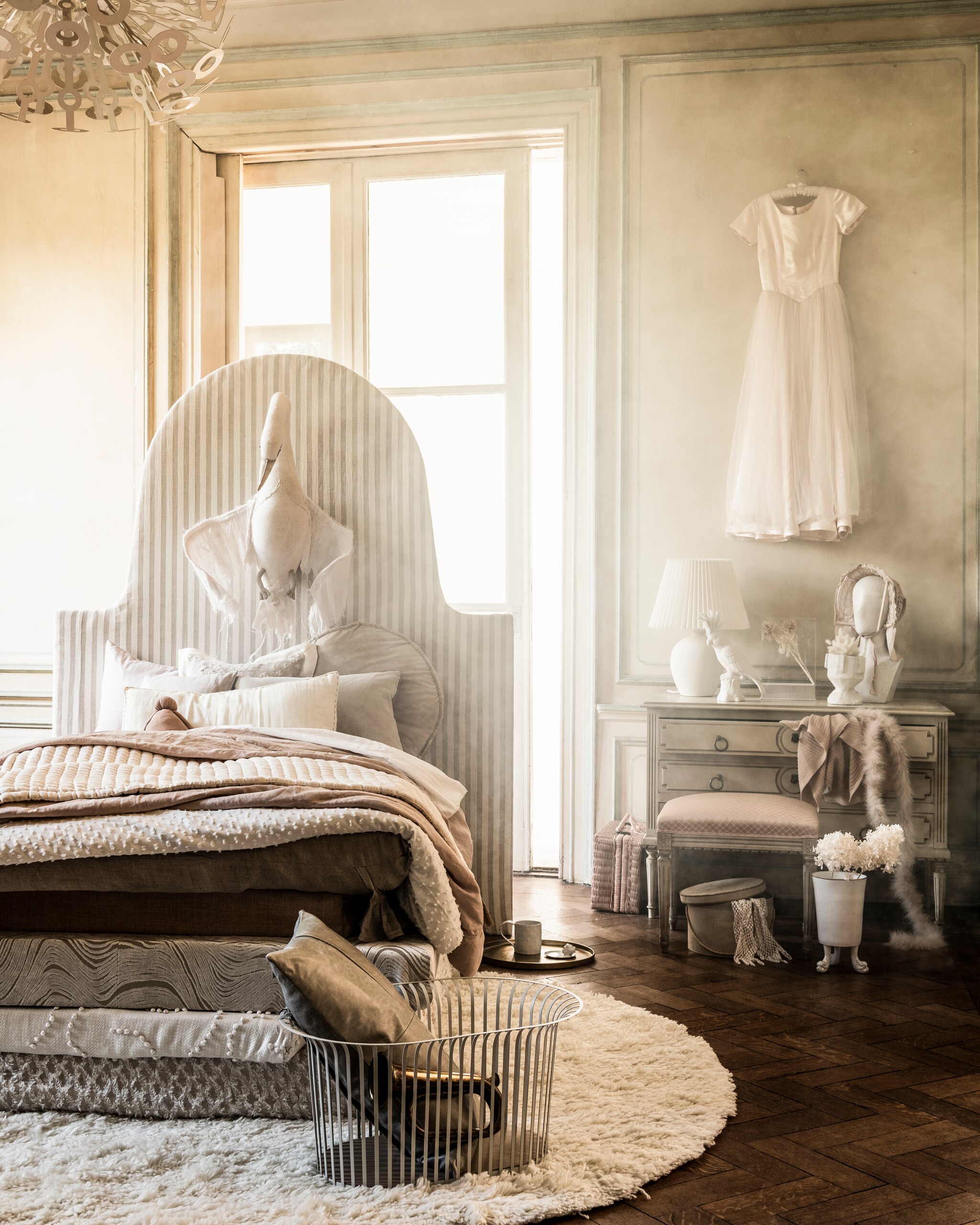 Matrassen en hoofdbord prijs op aanvraag (com-anders.nl). Stoffen op bed: linnen met streep Endless Summer Barbara Osorio per meter € 139,-, linnen in zalmkleur Valloire Designers Guild per meter € 85,-, linnen met golfmotief Aurelia Designers Guild per meter € 170,-, linnen met bolletjes Yotis Anatolia Nobilis per meter € 225,-,linnen met opengewerkt ruitmotief Kerouan Phoenicia Nobilis per meter € 104,-,linnen kussen met gaten Theia Nobilis € 238,-, langwerpig velours kussen € 88,- (wva.nl). Dekbedovertrek van wit plumetis € 69,99, zalmroze dekbedovertrek € 69,99, witte kap op schemerlamp € 29,99 (hm.com). Hanglamp privébezit. Rond kussen van HKliving € 64,95, rond kleed Vantaa van Linie Design 200 cm (Ø) € 495,-, gouden dienblad Palace van Salt &amp; Pepper € 39,95, witte kaketoe van Pols Potten € 59,-, vierkante stolp van HKliving € 89,95 (vtwonen.nl). Metalen mand € 210,- met daarin kussen € 135,-, kussen links op bed € 105,- (homestede.nl). Blaasinstrument € 20,-, hoedendoos € 35,- (harlequin-lisse.biz). Witte mok, per stuk € 99,-, schotel met hoofd erop € 75,-, vaas op pootjes € 332,- (maisonnl.com). Droogbloemen (judithslagter.nl). Vintage jurk € 225,-, lange handschoenen € 15,-, verenslinger € 45,- (lauradols.nl). Hoofd met hoed € 150,- (prinsheerlijkantiek.nl). Ladenkast € 325,- (burbri.nl). Kruk € 65,- (vandijkenko.nl). Rieten koffer € 85,-, zwaan € 595,-, roze knuffel in bed € 45,-, langwerpig kussen € 22,-, wit plaid € 90,-, zalmkleurig plaid uit ladekast € 90,- (archive-store.nl). Handgemaakte, witte vaas op kast prijs op aanvraag (babetteswereld.com). vtwonen 10-2021 |  styling Liza Wassenaar | fotografie Sjoerd Eickmans | assistentie Kula Isabelle van den Broek | bloemstyling Judith Slagter