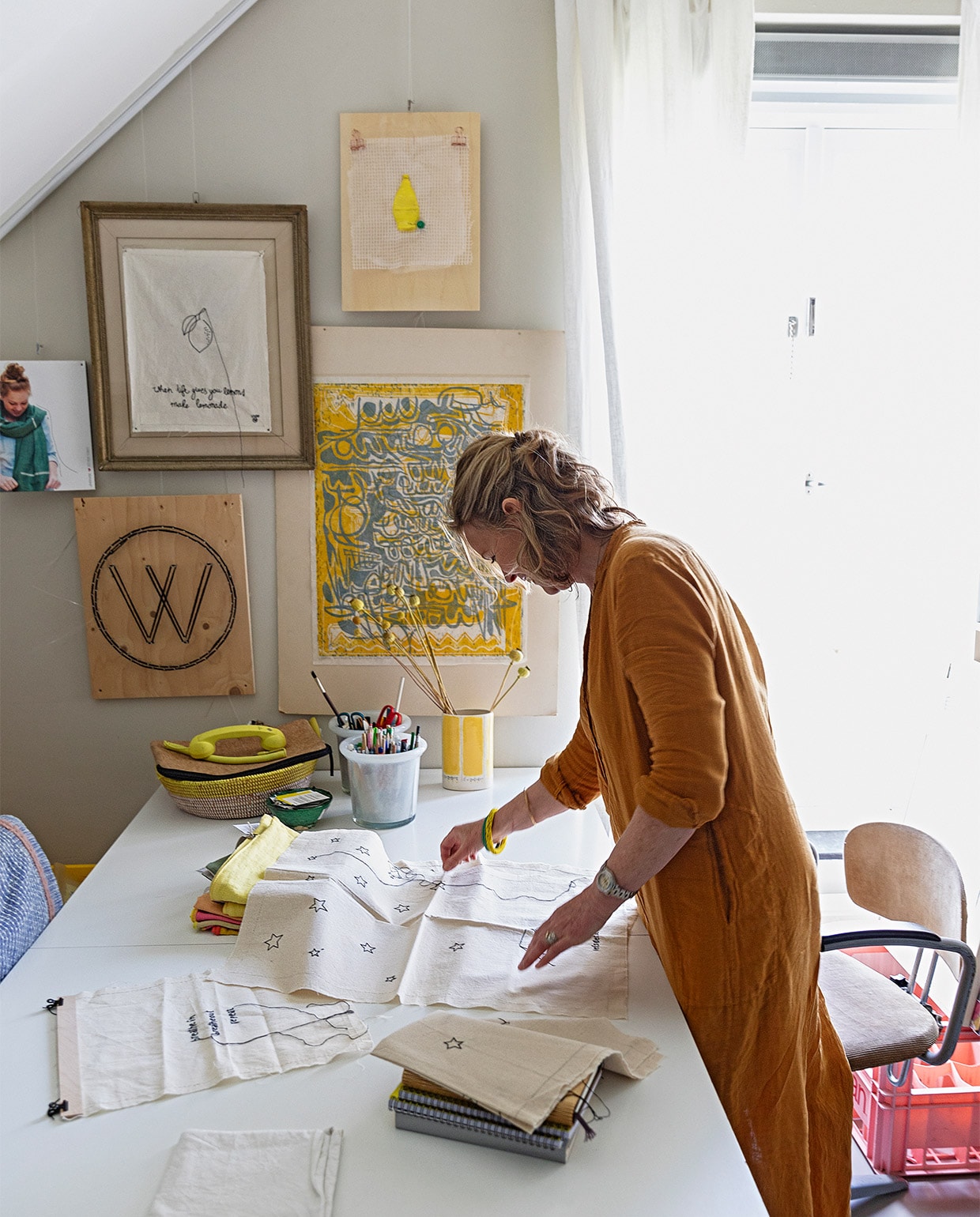 Karen in haar werkkamer op de eerste etage. Eames-tafel Vitra. Potten Rivièra Maison. Gele vaas gekocht bij een sociale werkplaats. Mand meegenomen uit Zuid-Afrika. Telefoonhoorn Native Union. Aan de muur hangen (met de klok mee) een citroenkunstwerk dat Karen maakte van plastic afval, een werk van Antoinette Gispen, het beeldmerk van Lemonwise (de W) en een geborduurde leus: If life gives you lemons, make lemonade. Foto visual merchandising Lemonwise. Stoel Marktplaats. vtwonen 07-2021 | styling Ilona Jongepier | fotografie Dana van Leeuwen | tekst Erik Paul Jager