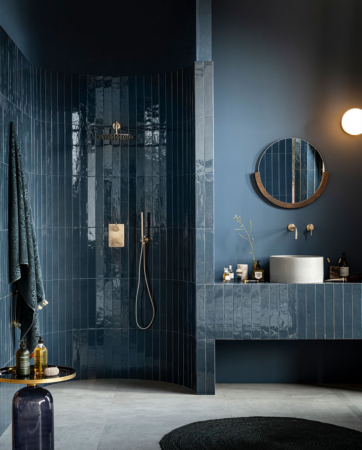 Wasmeubel en douchenis: wandtegel Marrakesh in kleur Ocean Blue, glans (ook in mat), 6,5×40 cm, per m² € 62,35. Op de vloer: vloertegel Raw in kleur Grey, 80×80 cm, per m² € 65,-. | M.m.v. vtwonen.nl (spiegel Mira van Umbra, vloerkleed Eternal van Ferm Living, wandlamp tr bulb van Menu), zarahome.com (handdoek), tegeldepot.nl (betonnen opbouwwaskom van Salenzi, inbouwwastafelkraan Slim Twenty van Wiesbaden, rvs doucheset van Wiesbaden), karwei.nl (bijzettafel Soof). Overig privébezit. vtwonen 11-2021 | productie Tanja Saarberg |  styling Kim van Rossenberg | fotografie sjoerd eickmans