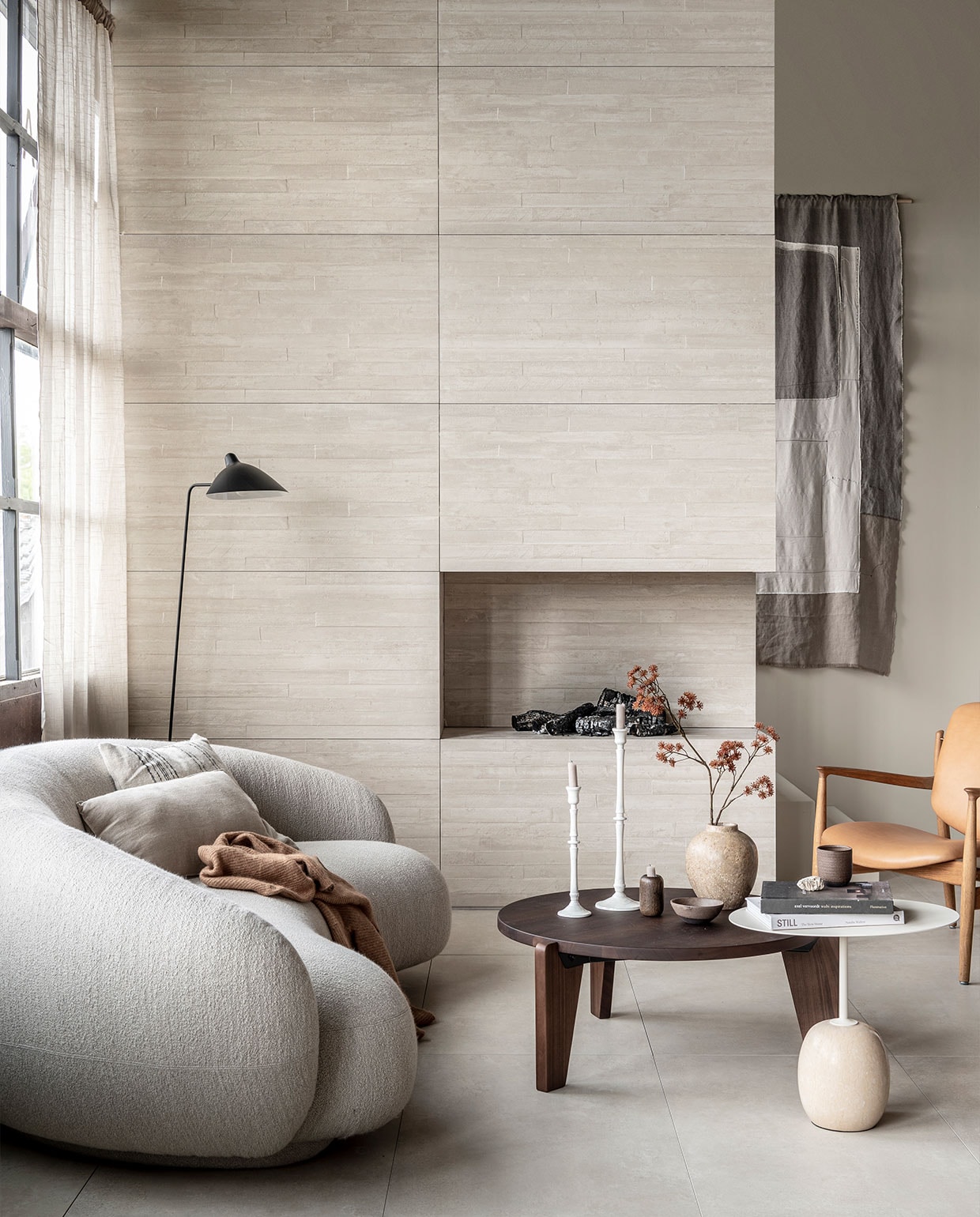 Op de wand: wandtegel Raw Casa Decor 3D in kleur Sand, 60×120 cm, per m² € 69,-. Op de vloer: vloertegel Raw in kleur Sand, 60×120 cm, per m² | M.m.v. justhaasnoot.nl (staande lamp, bank Julep van Tacchini, salontafel Guéridon Bas van van Vitra, witte bijzettafel Lato van &amp;Tradition, fauteuil van hout met leer van House of Finn), zarahome.com (witte metalen kandelaars, stenen vaas), suhka.nl (textielkunstwerk, kom en mok). Overig privébezit. vtwonen 11-2021 | productie Tanja Saarberg |  styling Kim van Rossenberg | fotografie sjoerd eickmans