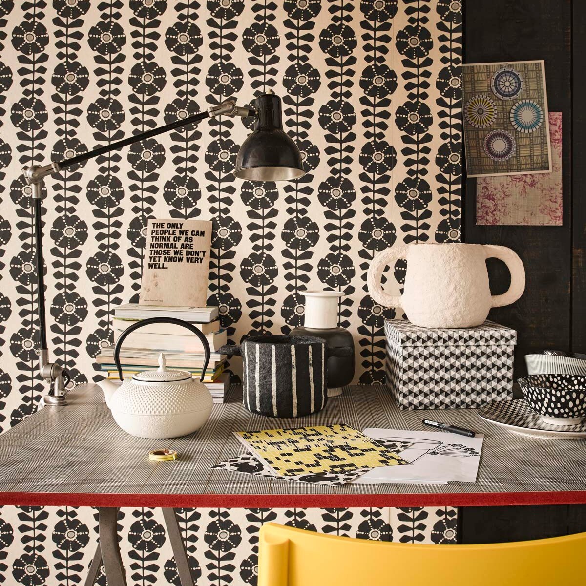 Behang Black &amp; Light met grafische bloemenprint, tafelblad beplakt met behang Atlantic (Eijffinger). Gele kunststof stoel, schragen (Ikea). Zwarte bureaulamp (Neef Louis). Witte Japanse theepot, zwart-witte pot papier-maché, witte pot met oren, vaas zwart-wit, doos, bord, kom zwart-witte stip, beker met streep (Loods 5). vtwonen 07-2018 styling Fietje Bruijn, fotografie Alexander van Berge
