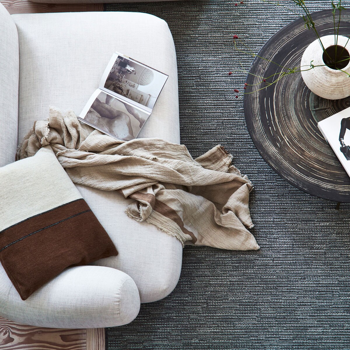 Wollen karpet Nature cord antraciet melé vanaf € 735,- M.m.v. letoile.store (bruin-wit kussen, plaid), homestede.nl (salontafel), zarahome.com (keramieken vaas op bruine salontafel, stenen vaas op bank met gevlochten zitting, houten opbergbox, slippers), homestede.nl (houten bank met gevlochten zitting), vantil.nl (voetenbank), sissy-boy.com (kom). Overig privébezit. Beeld: productie Tanja Saarberg | styling Danielle Verheul | fotografie Sigurd Kranendonk | assistentie sanne ketelaar