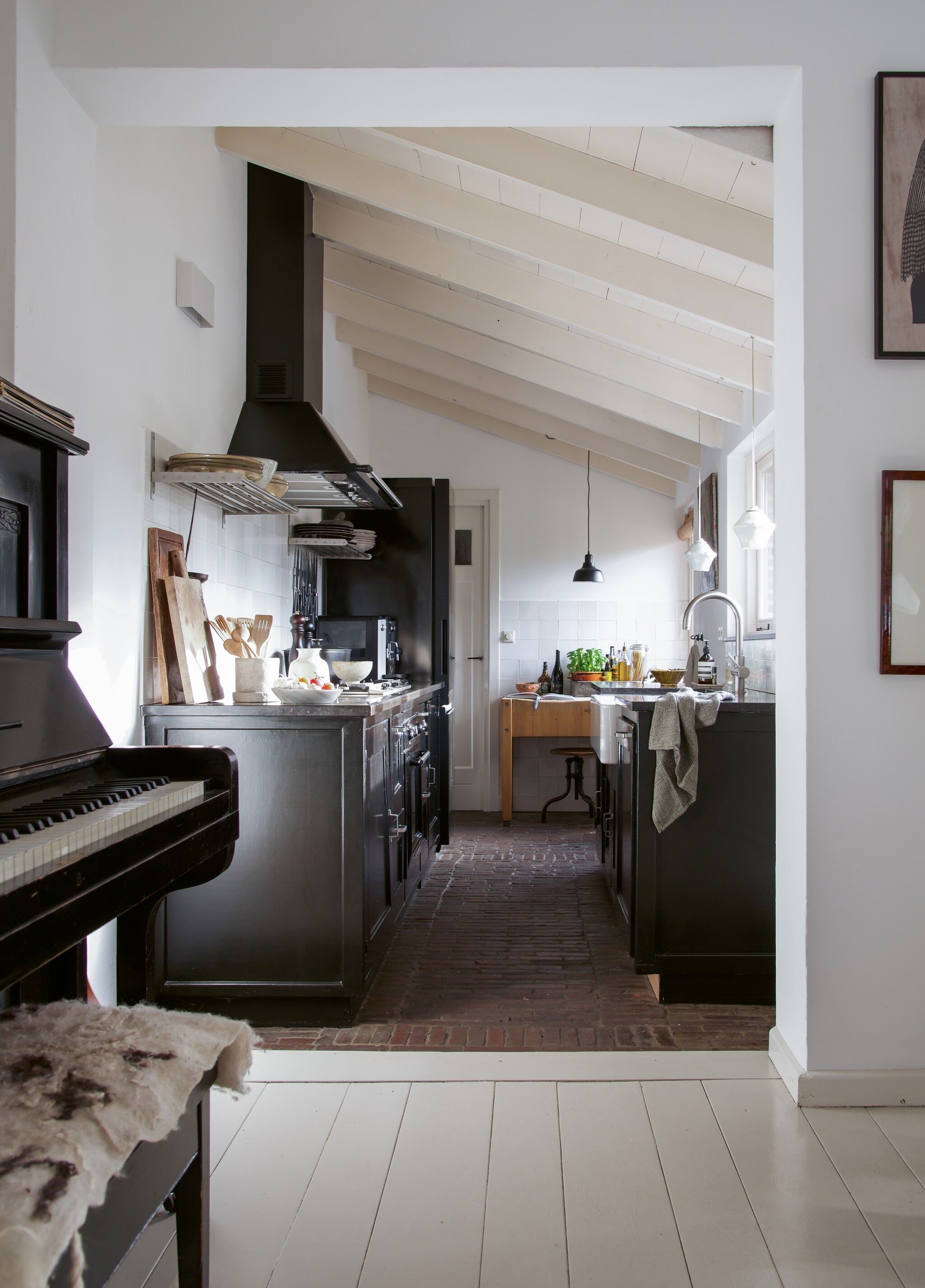 Keuken zelfgemaakt. Vloer van klinkers uit de tuin. Accessoires uit de schuur van Kris’ ouders. Op de wand oude Friese Witjes. Piano Van Urk Rotterdam. Lampen herkomst onbekend. vtwonen 09-2021 | Styling José Spaans | Fotografie Barbara groen | Tekst Anne van den Dool