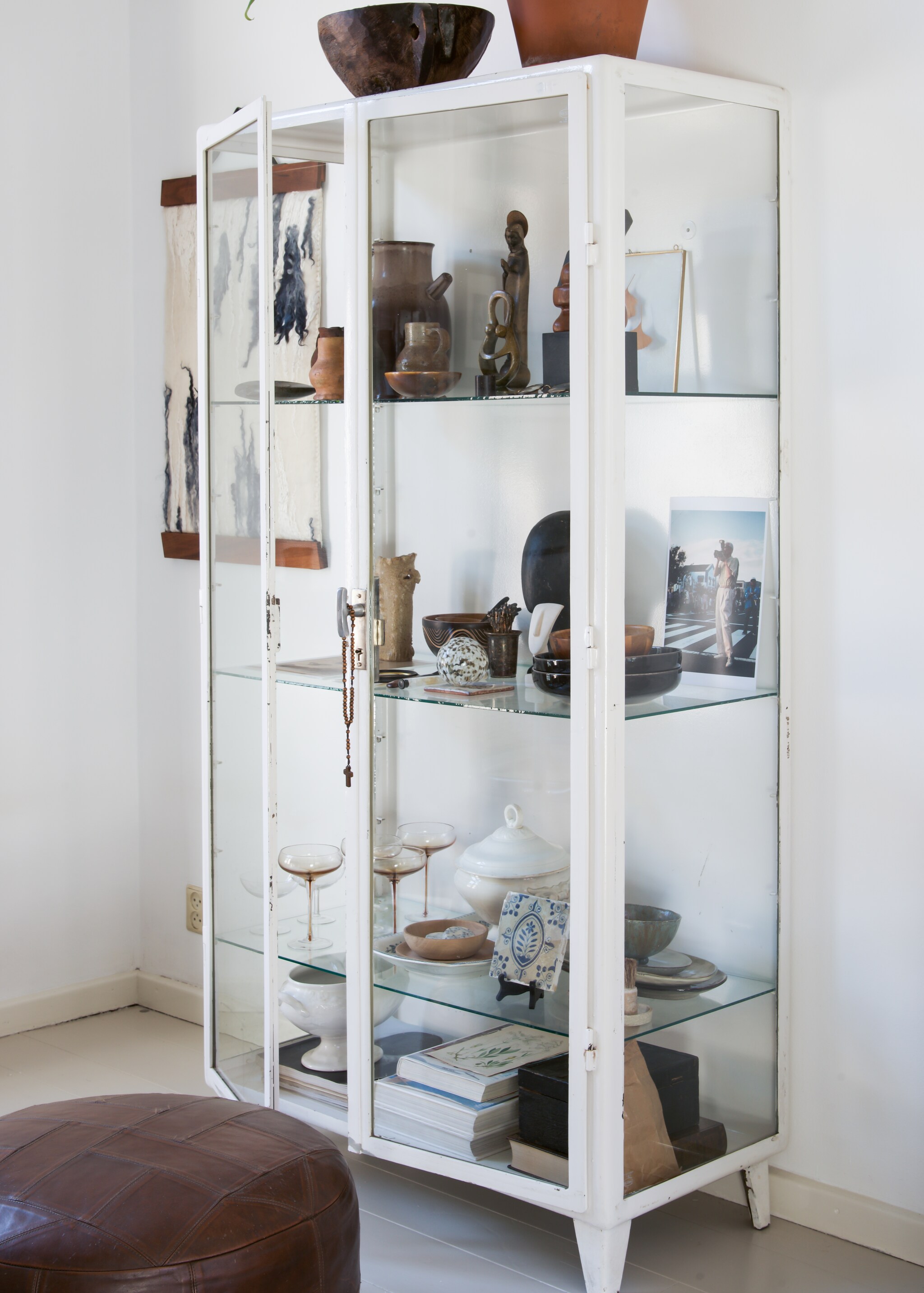Poef kringloopwinkel. Vitrinekast Vintage Fabriek. Schaal herkomst onbekend. Houten schaaltjes uit Afrika. Klein hoofd kringloopwinkel. Groot hoofd HKLiving. Tegel uit Portugal. Overig herkomst onbekend. vtwonen 09-2021 | Styling José Spaans | Fotografie Barbara groen | Tekst Anne van den Dool