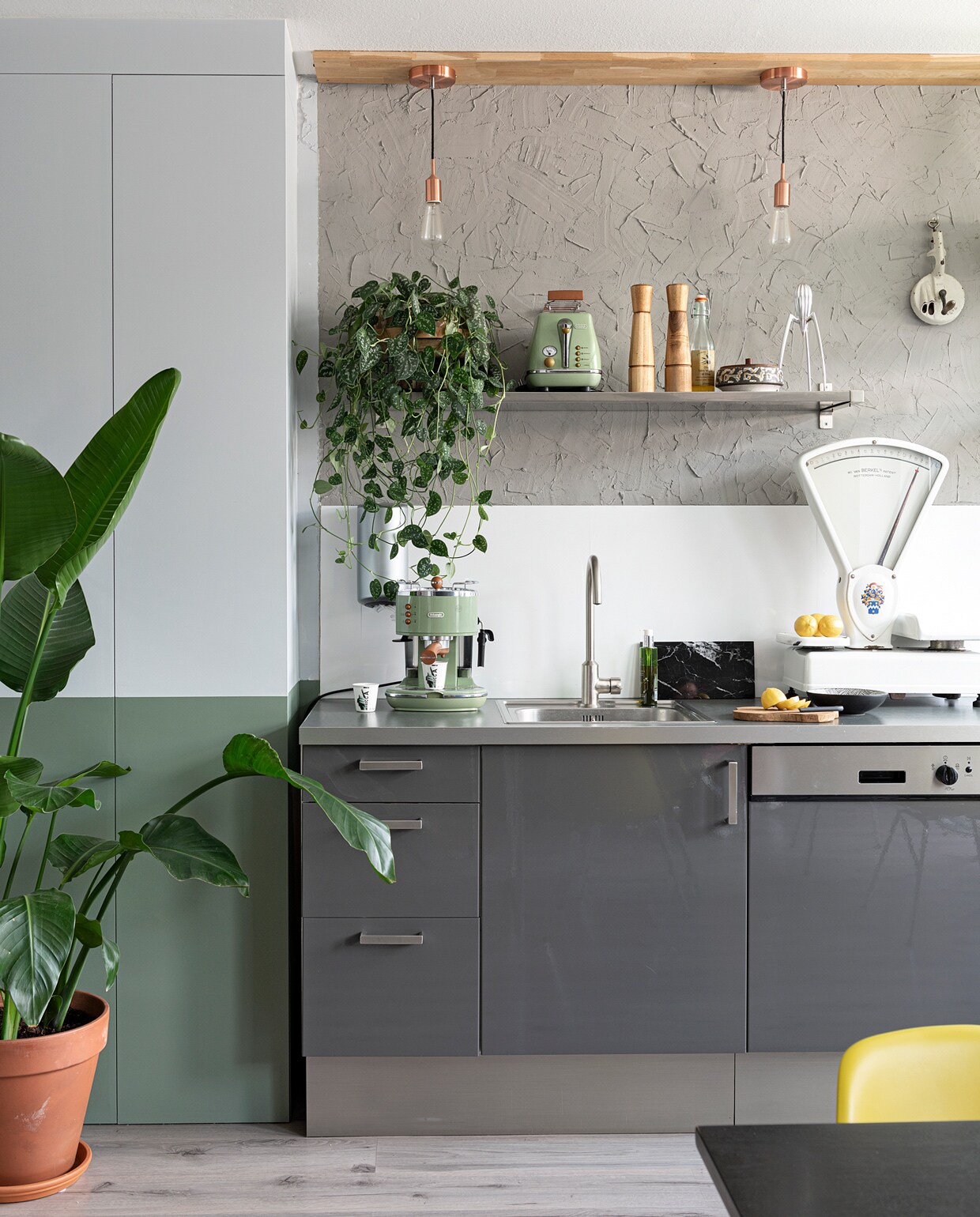 Muurkast zelfgemaakt, kleur zinkgrijs en leemgroen Karwei. Keuken en plankje Ikea. Achterwand keuken boerenstuc zelfgemaakt. Hanglampen Karwei. Op de plank: broodrooster De’Longhi via Mediamarkt, peper- en zoutstel Ikea, olijfolie supermarkt, potje met deksel kringloop, sinaasappelpers Alessi via Flinders. Aan de muur links: Plenty Easypull Dispenser via Blokker, rechts bonensnijder van de rommelmarkt. Weegschaal rommelmarkt, koffiezetapparaat Icona van Delonghi, kopje Il Coccio, marmeren plank Stoned, houten plank Xenos, zeeppompje Rituals. Plantenpot Intratuin. vtwonen 09-2021 | styling Sharon Roest | fotografie Caroline Martinot | tekst Sara Madou