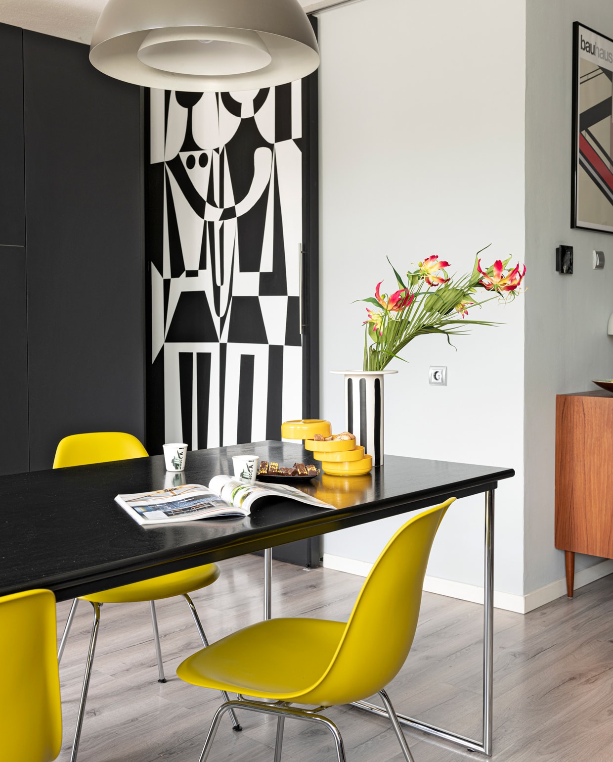 Muur zinkgrijs Karwei. Lamp Arne Jacobsen, tafel Gispen, gele stoelen Vitra Eames, kastje en gele bakjes Marktplaats. Vloer Ikea. Zwart-wit beschilderde schuifdeur zelfgemaakt. Vaas Loods 5, kopjes Il Coccio. vtwonen 09-2021 | styling Sharon Roest | fotografie Caroline Martinot | tekst Sara Madou