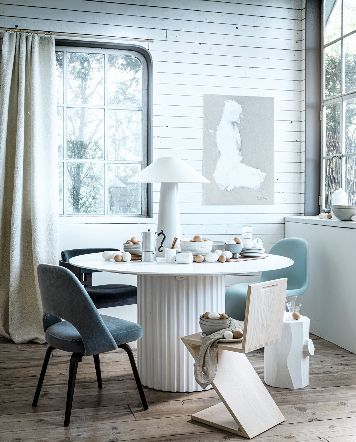 Gordijnstof Frimas in kleur Ivoire van Nobilis (wva.nl). Ronde eettafel, 140×75 cm (Øxh), tafellamp, lampenkap (hkliving.nl). Blauwe fluwelen stoel met houten poten, houten stoel met fluwelen zitting (edha-interieur.nl). Lichtblauwe stoel, grijs schaaltje op poten (loods5.nl/design). Witte kruk (nrdrhvn91.nl). Houten zigzag stoel (homestede.nl). Houten borden, zachtblauwe kommen, houten lepels, zachtblauw borden, houten snijplank (hm.com). Koffiepotje, witte glazen met zwart randje (stadspaviljoennoord.nl). Witte porseleinen kreukbekers van Serax, grijze dinerborden met beige rand van Serax, grijze schaal met beige rand van Serax, grijze kommen met beige rand, linnen theedoek van vtwonen, glazen van Serax, set van 4 klein, groot (vtwonen.nl). Witte schalen met zwarte spikkeltjes (loods5.nl). Witte toren van seleniet (tinekhome.com). Geschilderde poster (theodeto.com). Overig privébezit.