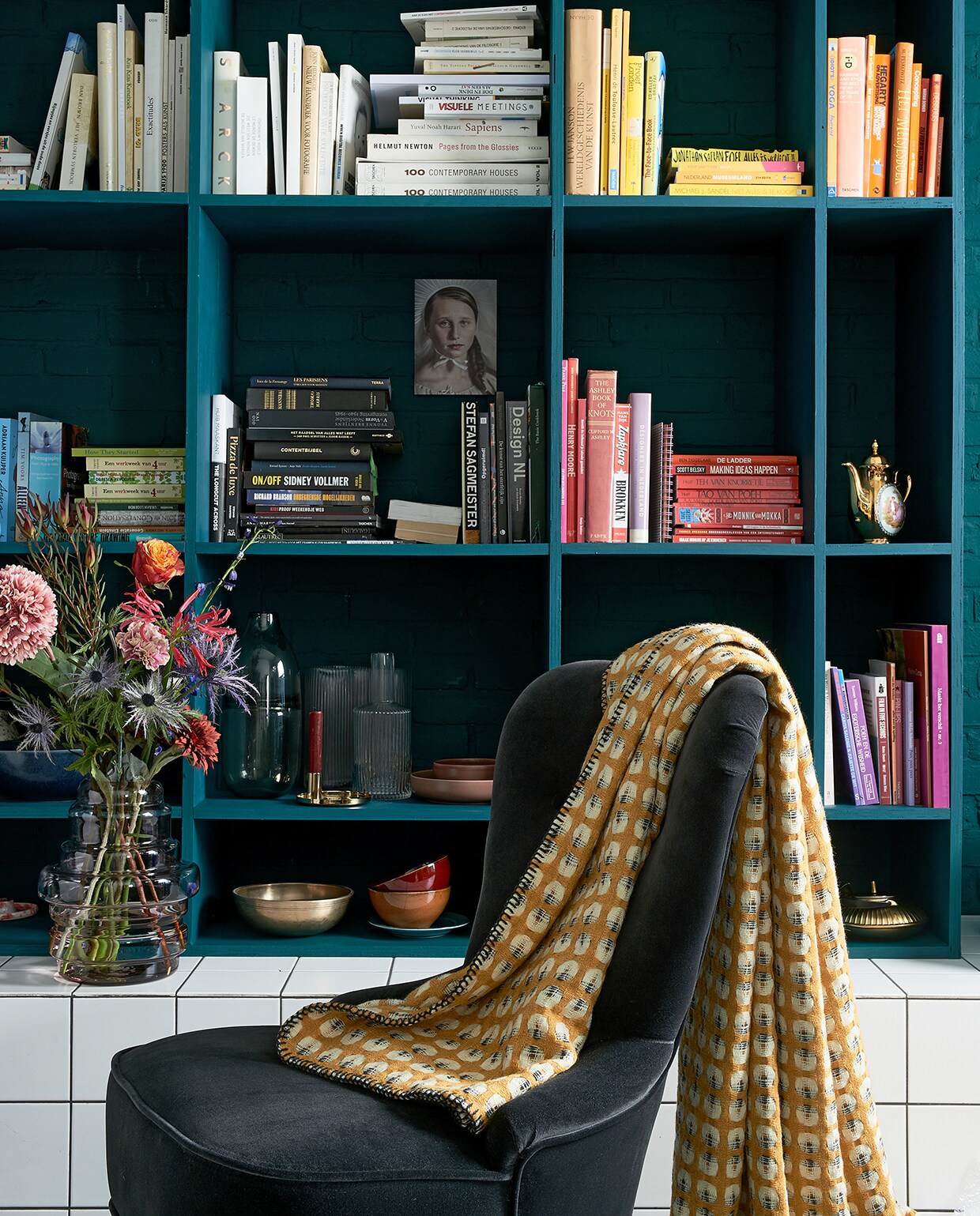 Boekenkast in kleur Marina Blue matte lak (Little Green). Fluwelen stoeltje Remsta (ikea.nl). Plaid Klara (made.com). Rood kommetje, mat gouden theepot. Grijze glazen vaas Rubygrey. Geribbelde vaas Hilmir, vaas Manfred. Kunstbloemen v.a.. Foto vrouw (racheldubbe.com). Overig privébezit. vtwonen 03-2020 | Styling Fietje Bruijn | Fotografie Dennis Brandsma