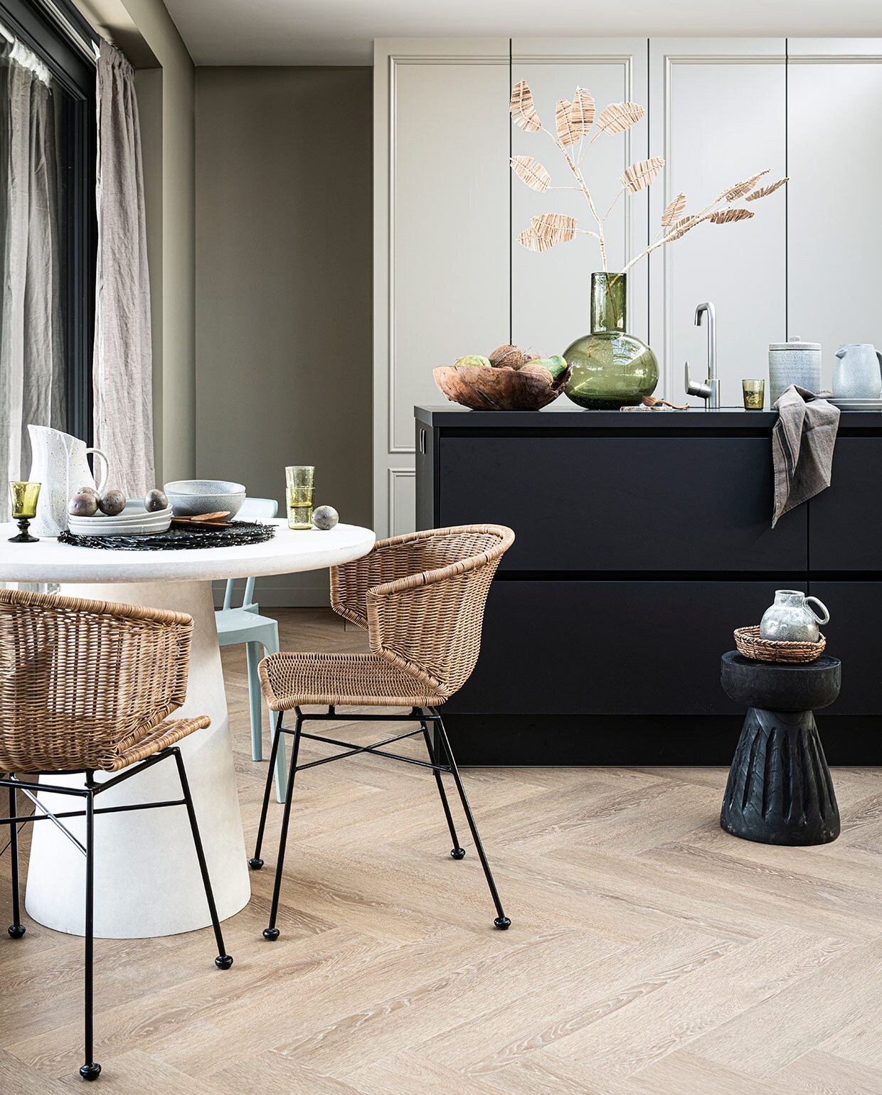 PVC Vloer Herringbone Sun Kissed, visgraat 76,5×15,3 cm dryback per m² € 44,95, 75×15 cm click per m² € 57,95. Ook in de kleuren Natural, Polar en Roasted. M.m.v. basiclabel.nl (eettafel, eetkamerstoelen en houten kruk van Woood), vtwonen.nl (grijze borden, schalen, kom, placemats, stenen pot met deksel, kruik met handvat, alles van Bloomingville), sissy-boy.com (grijze kan wit geverfd, houten schaal, rotan takken), hm.com (mand, linnen gordijn), paviljoennoord.com (groen wijnglas, groene waterglazen, houten bestek, groene glazen vaas, theedoek). Overig privébezit. vtwonen 06-2021 | Productie Tanja Saarberg | Styling Danielle Verheul | Fotografie  Sjoerd Eickmans