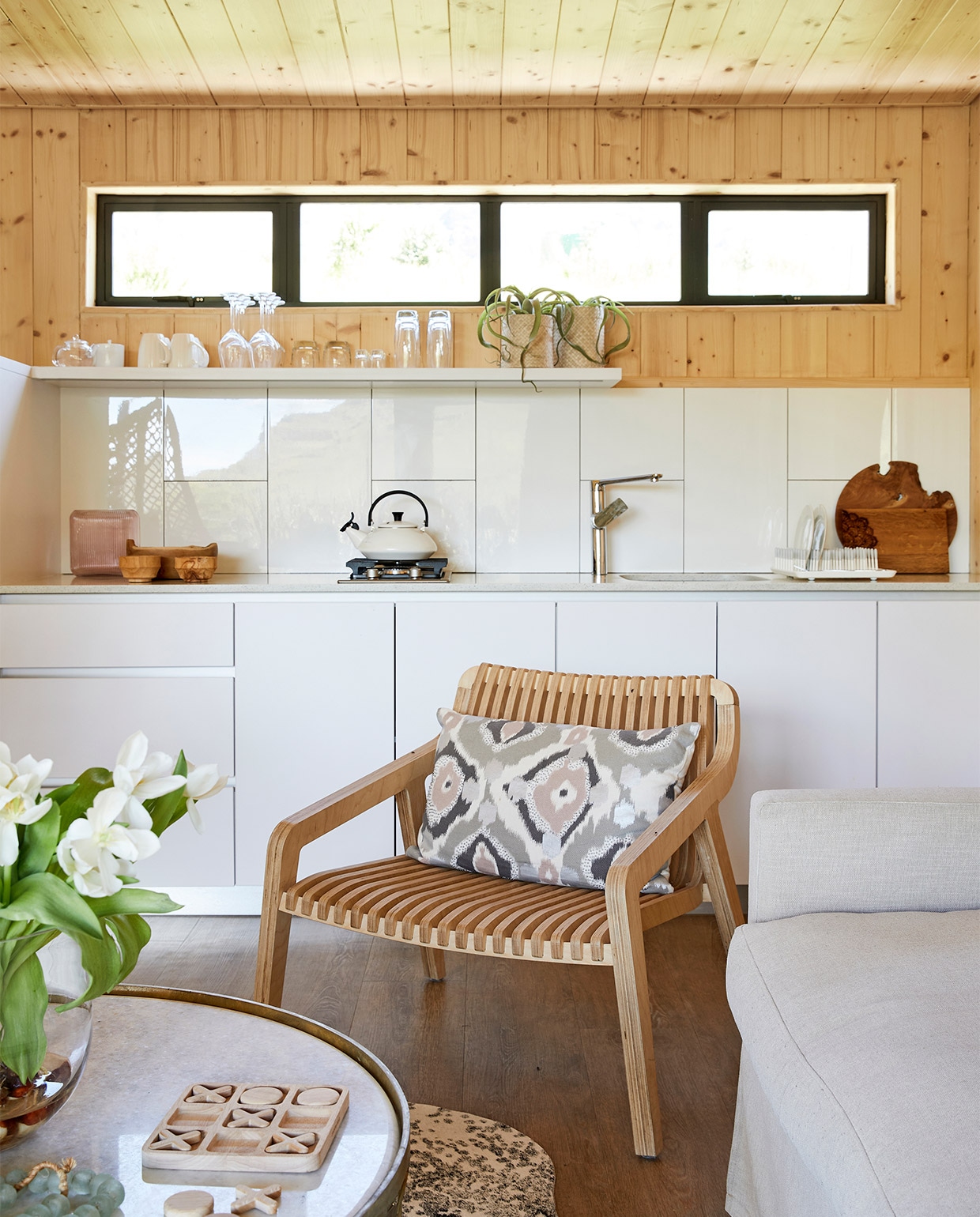Kim koos voor witte, glanzende tegels en melamine kastjes. In het blad is gerecycled glas verwerkt. Kraan Hans Grohe. Keukenblad ProQuartz. Houten fauteuil Radius Minima. Koeienhuid African Leather and Skins. Salontafel Coricraft. Overig onbekend. vtwonen binnenkijken special 171-2021 | styling Sven Alberding | fotografie Warren Heath/Bureaux