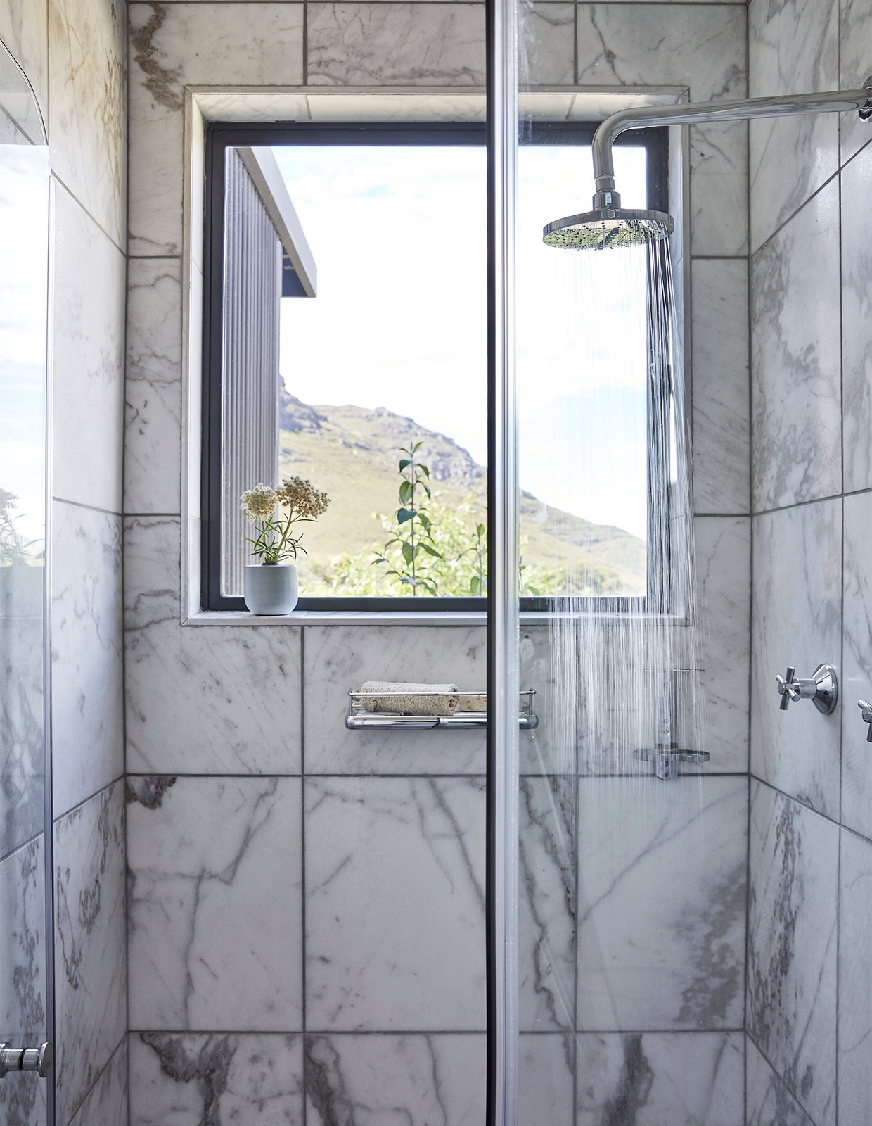 Zelfs vanuit de douche kijk je uit op de bergen. Marmeren wandtegels Mugula Storm Artmar. vtwonen binnenkijken special 171-2021 | styling Sven Alberding | fotografie Warren Heath/Bureaux