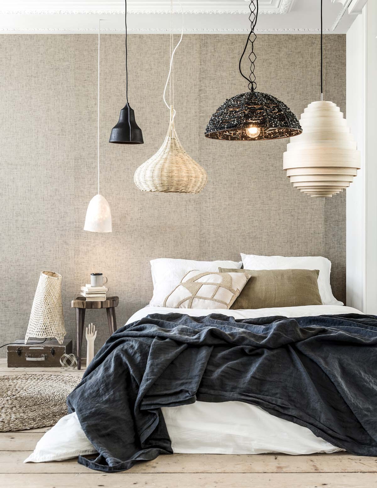 Op de koffer organische rieten tafellamp (HKliving). Boven de kruk Felted Lamp Long van wol, bamboe hanglamp Union, rechts hanglamp AY Illuminate Urchin Tall, zwarte linnen sprei, wit linnen dekbedovertrek, bruine kussenhoes (Couleur Locale). Zwarte leren hanglamp Art Lloyd (Puik). Zwarte hanglamp van kralen Ehsan Distressed, roze kussen met kralen Hasani Beaded Cushion, mok Earth Mug Graphite (Dassie Artisan) Behang naturel 322610 (Eijffinger). Houten hand (Hay). Kruk Pads van walnoothout (De Machinekamer). Jute karpet Round Natural (By-Boo). Overig privébezit. vtwonen 10-2018 | Fotografie Sjoerd Eickmans | Styling Marlies Does