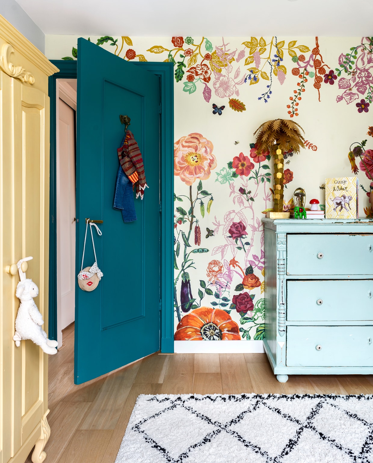 De kleurrijke kamer van Guusje. Behang van Nathalie Lété. Blauw kastje van Van Dijk en Ko. Palmboomlamp van HK Living. De gele kast stond al in het huis, Sophie verfde hem in Sudbury Yellow van Farrow &amp; Ball. Kleed Karwei. De deur is geschilderd in de kleur Vardo van Farrow &amp; Ball. vtwonen special binnenkijken 12-2019 | styling Lindividu | fotografie Stan Koolen, CocoFeatures
