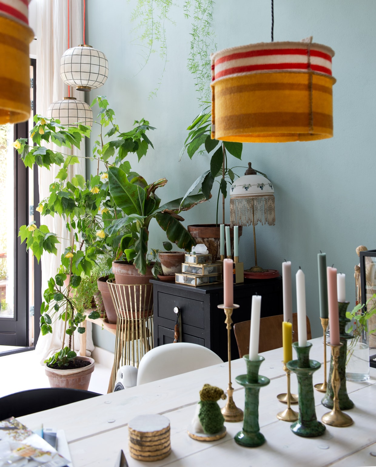 Tafel van Jorg Steigerhout. Erop een groene Tamegroute vaas en kandelaren van World of Blends. De bank hebben Jet en Michiel op maat laten maken bij oudisnieuw.net. Oranje kussen kelimshop.nl. Tulip Chair van Eero Saarinen en witte Panton Chair via Marktplaats. Hanglampen Woollight van beeldenbouwers.nl. Zwart geverfde oude commode. Glazen doosjes Sissy-Boy Homeland. Lamp met franje uit Antwerpen. Parelmoer met messing hanglamp ouders Michiel. Muurverf kleur Lianne van Fairf. vtwonen 12 binnenkijken special 2019 | Styling Jet van der Graaf | Fotografie Trui Heinhuis | Tekst Caroline Westdijk