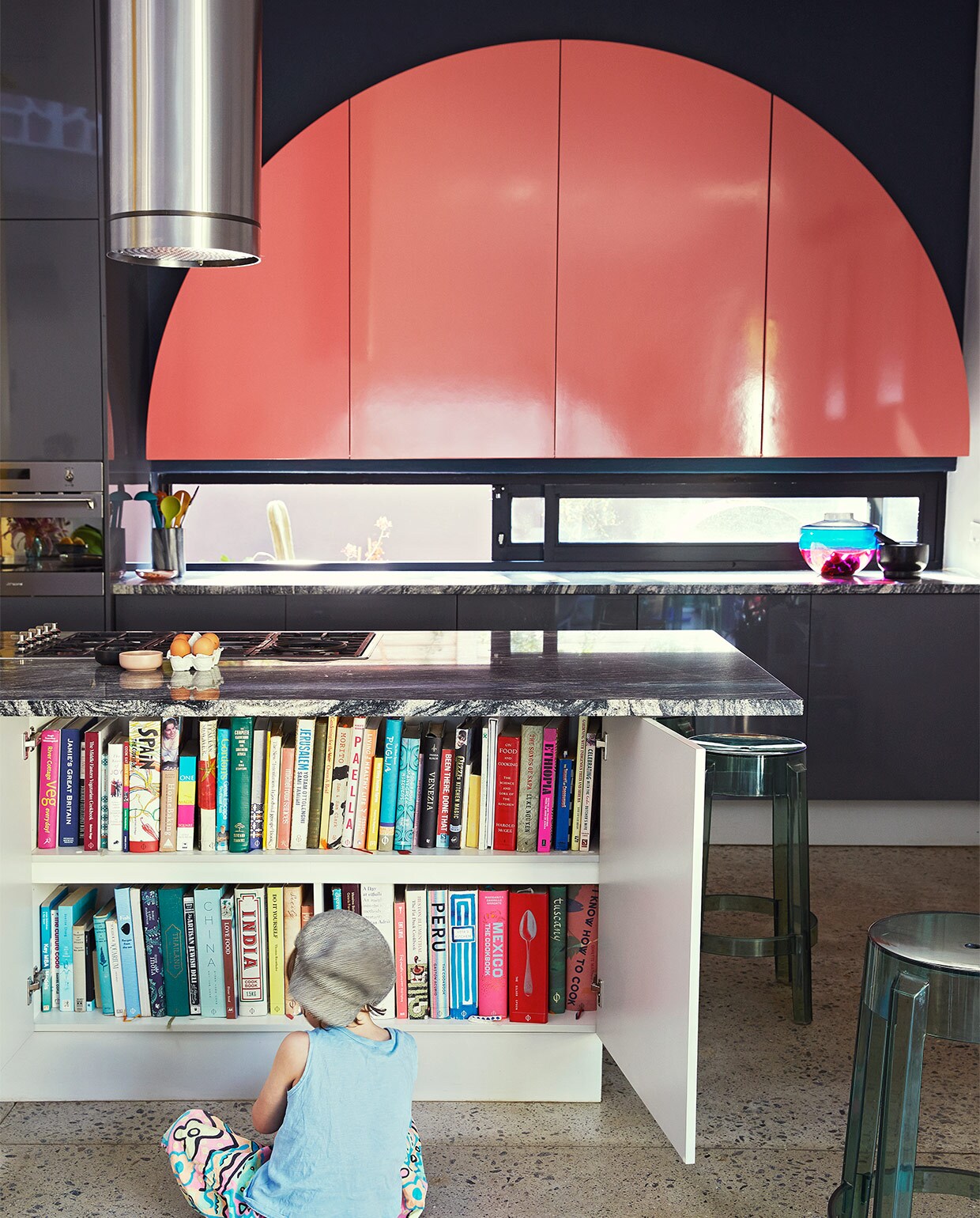 Keuken ontworpen door Gregory Katz via ProReno Kitchens, met werkblad van Namibisch graniet International Slate Sales. Vloer gepolijst beton World of Decorative Concrete. Barkrukken Charles Ghost en blauw-roze vaas Shibuya Kartell. Zwarte haken Leroy Merlin. vtwonen binnenkijk special 07-2021 | productie Livinginside/Bureaux | fotografie\nElsa Young