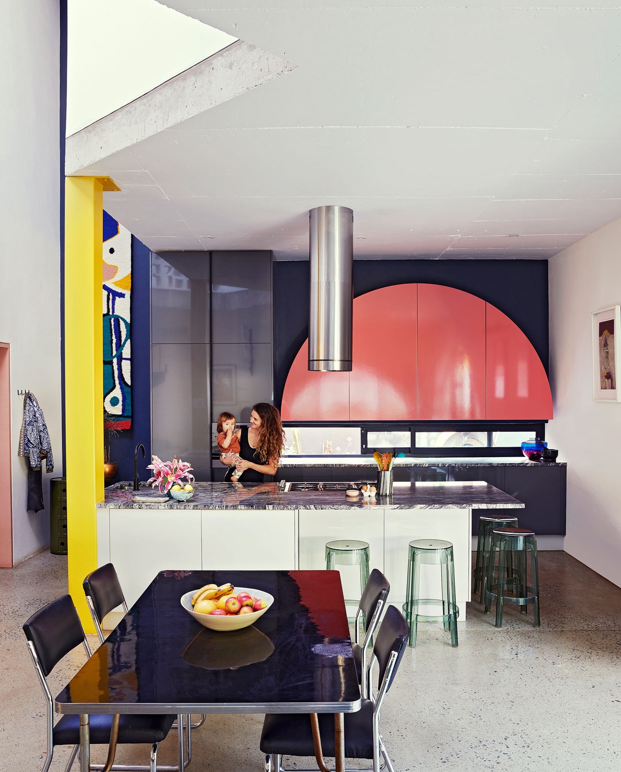 Keuken ontworpen door Gregory Katz via ProReno Kitchens, met werkblad van Namibisch graniet International Slate Sales. Vloer gepolijst beton World of Decorative Concrete. Groene bijzettafel Componibili, barkrukken Charles Ghost en blauw-roze vaas Shibuya Kartell. Eettafel en chromen buisstoelen vintage. Fruitschaal Wonki Ware. Zwarte haken Leroy Merlin. Wandkleed Renée Rossouw. vtwonen special binnenkijken 06-2021 | productie Living Inside, Bureaux | fotografie Elsa Young