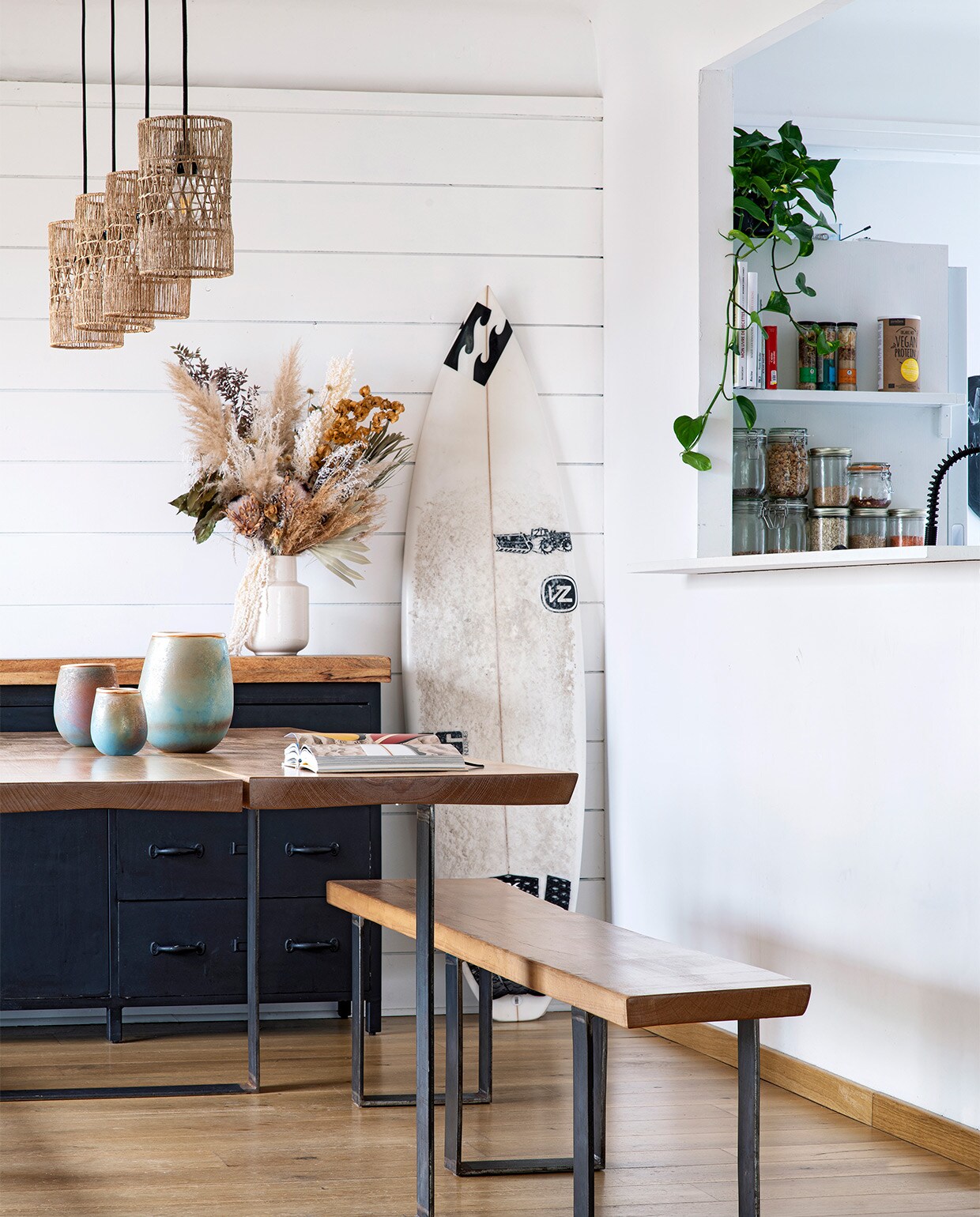 Houten tafel en bank door Sam gemaakt. Keramiek verzameld in Frankrijk. Grijze vaas Ikea. Droogbloemen Teepee Sauvage in Hossegor. Rotan lampen La Redoute. De surfplank was ooit van de Australiër Joel Parkinson, wereldkampioen surfen in 2012. vtwonen binnenkijk special 07-2021 | productie &amp; tekst Anne-Catherine Scoffoni | styling Catherine Cornille | fotografie Patrick Sordoillet