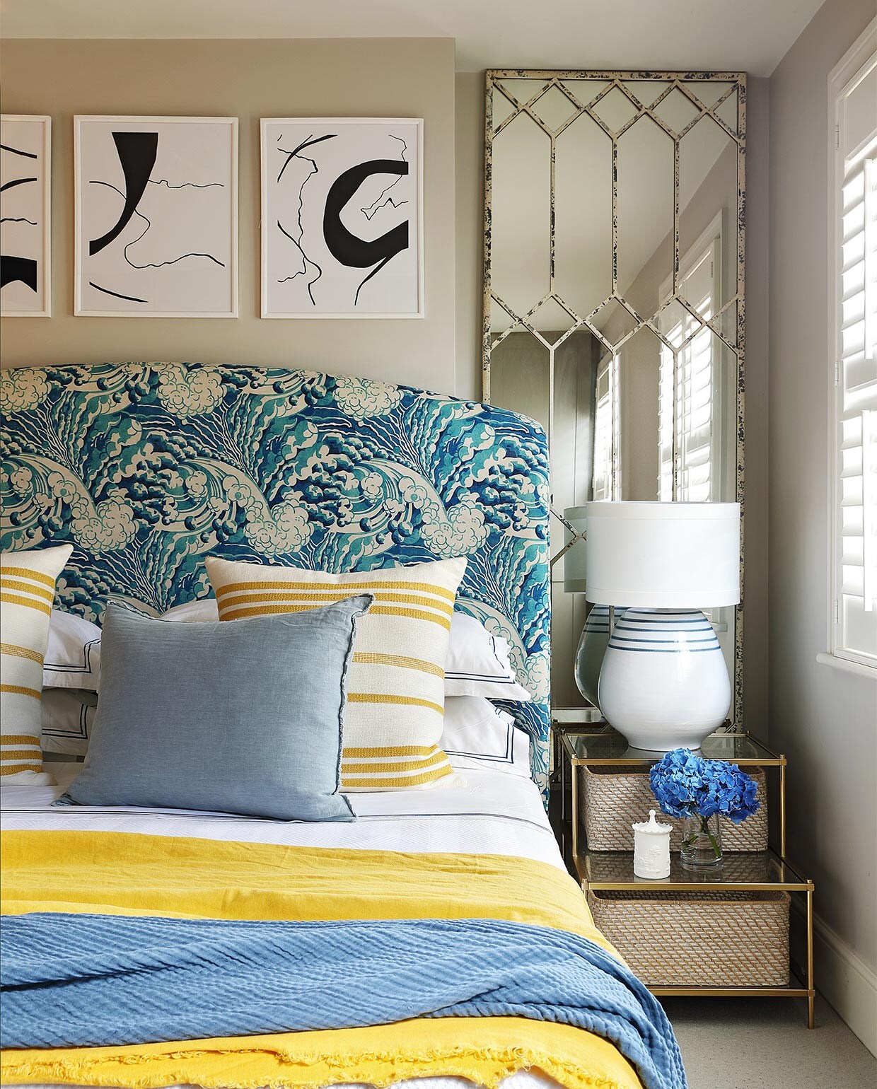 Muurverf Cornforth White van Farrow &amp; Ball. Het hoofdbord is bekleed met stof The Wave in de kleur mineral van Linwood Fabric. Beddengoed Granny Goose. Kussens met gele streep van stof Marina in kleur pastis van Lelièvre. Vaalblauwe linnen kussens lokaal gekocht. Gele en blauwe plaids H&amp;M Home. Spiegel Block &amp; Chisel. Tafellamp Gioalo van OKA. Bankje bekleed met stof van Mavromac. Kunst in lijsten gekocht via Etsy. vtwonen binnenkijk special 07-2021 | productie Sven Alberding/Bureaux | fotografie\nElsa Young