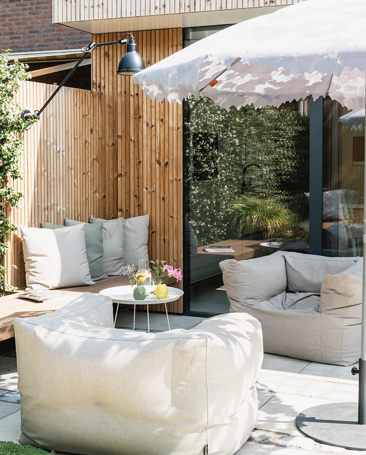 Latten rondom het huis thermo pine design rabat. Tuinstoelen Bryck. Op maat gemaakte kussens Sunbrella. Bijzettafel Fatboy. Parasol Droog. Hanglamp DCW Editions. Gele en groene vaas bloemenwinkel Jasmijn. vtwonen 08-2021 | fotografie Muk van Lil
