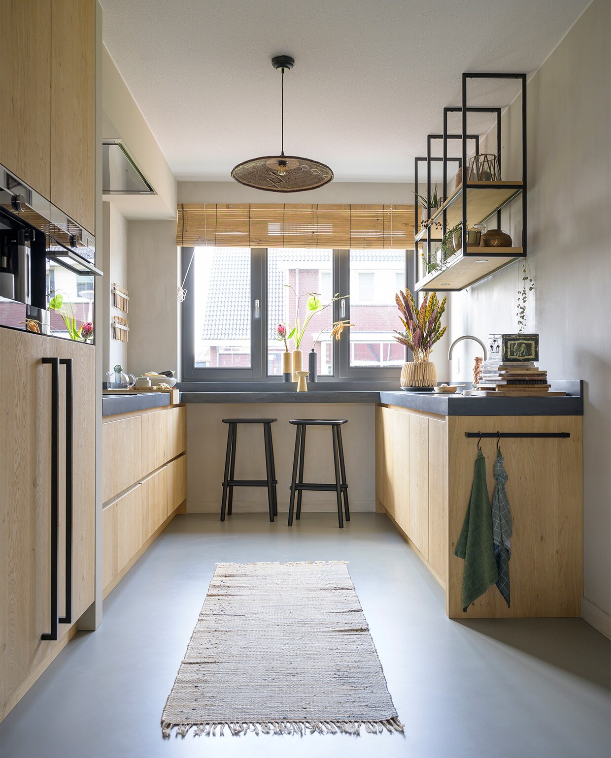 Zelfontworpen keuken Van Lieshout keukens &amp; interieur. Apparatuur AEG. Beton ciré werkblad Beal. Hanglamp Casa Gitane. Krukken Butt van vtwonen. Rolgordijn Bamboo Import Europe. Vazen op de bar erfstuk oma. Vloerkleed Madam Stoltz. Herkomst plantenpot onbekend. Theedoekenrek onderdeel van de keuken. vtwonen 08-2021 | styling José Spaans | fotografie Stephanie Driessen