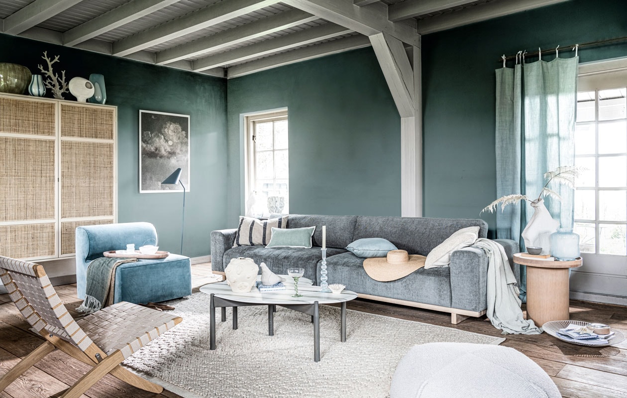 Krijtverf Polar Blue op de wand, per liter € 39,25 (pure-original.nl). Kast van HKliving, 125x40x200 cm (bxdxh) € 1495,- (vtwonen.nl). Grijze keramieken vaas € 255,-, witte glazen vaas met blauwe streep € 41,-, blauwe glazen vaas met witte cirkel € 99,-, blauwe glazen karaf € 42,- (brostecopenhagen.com). Koraal op voet € 150,-, marmeren salontafels, 115x60x 37 cm (;xbxh) en 73x62x 33 cm (lxbxh), set van 2 € 2199,- (vantil.nl). Witte keramieken vaas op voet met gat € 35,99, keramieken object stekel € 29,99, lichtblauwe glazen vaas € 29,99 (sissy-boy.com). Gevlochten fauteuil € 726,-, plaid met blauw-beige kleurverloop € 139,-, ovaal houten dienblad € 105,-, vloerlamp € 780,-, stoffen vogel € 45,-, poef € 230,-, witmetalen schaal € 65,-, houten opberger met glazen deksel € 45,- (homestede.nl). Blauw waterglas € 9,95, notitieboekje met bloemprint € 19,95, cocktailglas op gedraaide poot € 15,95, blauwe glazen kandelaar € 21,95 (anna-nina.nl). Witte vazen, per stuk vanaf € 80,- (lanenahome.com). Witte porseleinen theepot € 74,-, grijze kom € 13,50 (serax.com). Blauw-wit kunstobject vaas van Dum Keramik € 492,- kunstobject vaas met schelpen van Josefina Feurst € 352,- (theodeto.com). Fluwelen fauteuil van Menu € 1350,-, vloerkleed van Menu € 800,- (designtales.nl). Karton geprint met een detail van schilderij Botafogo Beach van Eduardo de Martino € 35,- (repros.nl). 4-zitsbank Aya, 318x96x79 cm (bxdxh) € 1299,- (sofacompany.com). Schilderij op canvas € 850,- (mooswillemsen.com). Blauw gestreept kussen € 19,99, turkooizen kussen met witte rand € 22,99, blauw kussen met donkerblauwe bies € 19,99, hoed € 39,99, gebroken wit kussen € 19,99, plaid € 35,99 (zarahome.com). Houten bijzettafel € 439,- (bolia.com). Gordijn gemaakt van stof Brera Lino van Designers Guild, per meter € 72,- (wva.nl). Overig privébezit. vtwonen 08-2021 | styling Danielle Verheul | fotografie Sjoerd Eickmans | assistentie Niels Kist, Meike LintHorst | maatwerk Meta Poulain