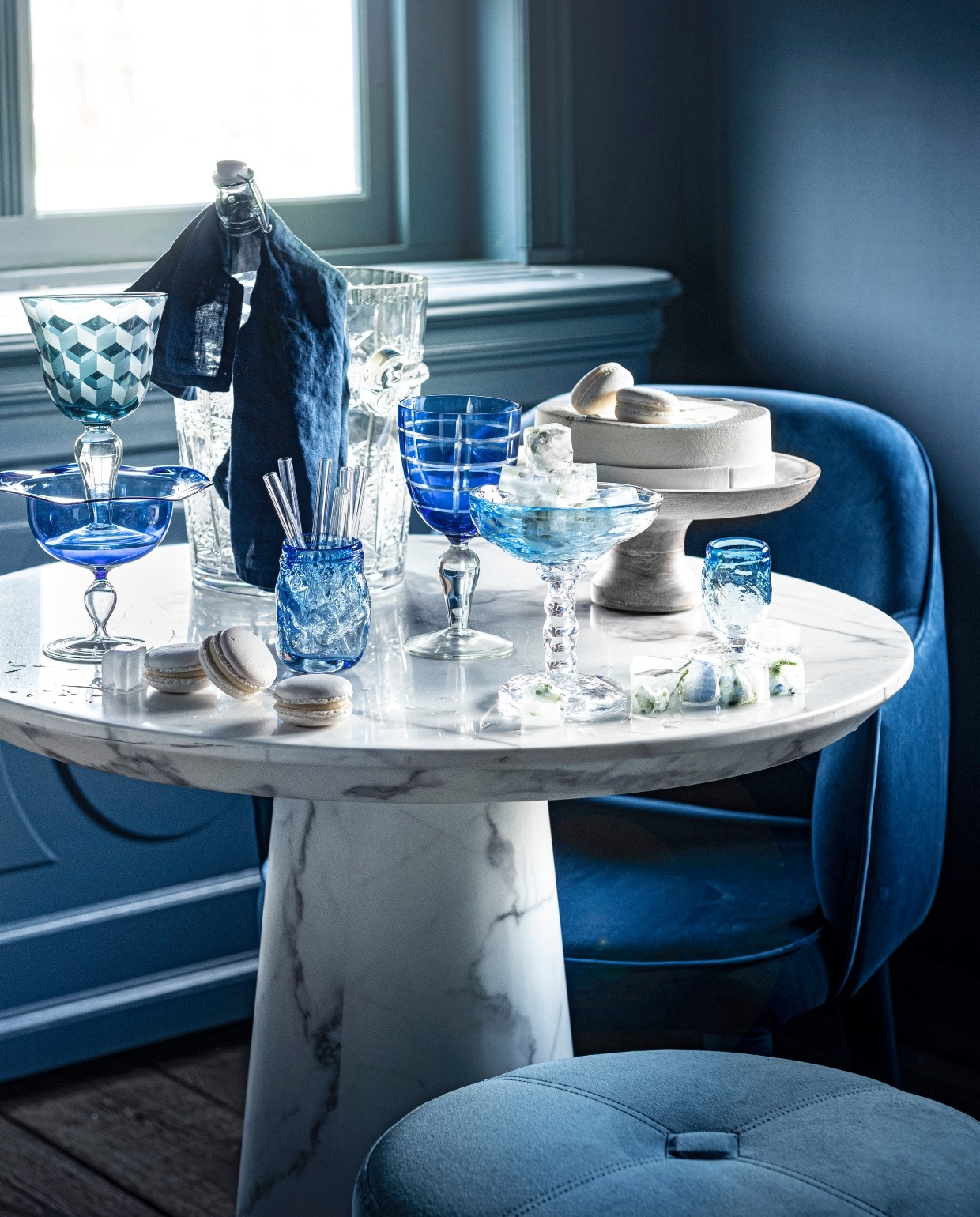 Poef van Minotti € 1150,-(covanderhorst.nl). Stoel Cosy van PolsPotten € 302,99 (vtwonen.nl). Wijnkoeler€ 175,- (pietjonker.nl). Blauw wijnglasmet print links, set van 6 € 129,-, blauwgestreept wijnglas in het midden, set van 6€ 129,- (polspotten.nl). Waterkaraf metdop, prijs op aanvraag (sostrenegrene.com).Blauw glas linksonder € 10,- (loods5.nl).Glazen rietjes, set van zes € 10,50(bijenkorf.nl). Taart gemaakt naar wens€ 32,95 (huizevanwely.nl). Gebobbeldglas € 30,-, gebobbelde ijscoupe metijsklontjes € 50,-, smal gebobbeld blauwglas € 20,-, linnen servet, set van 2 € 9,99(hm.com). Zelfgemaakte ijsklontjesmet blaadjes en bloemetjes erin. Overigprivébezit. vtwonen 07-2020 | styling Liza Wassenaar | fotografie Sjoerd Eickmans