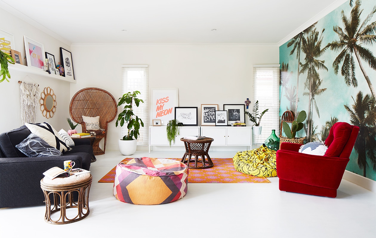 Palmbomen-behang Byron Bay Wallpaper. Yin-en-yangkussen, kussen Locals Only en regenboogkussen Kawaiian Lion. Grafisch zwart-witkussen Target. Macramé wandhanger Family Threds. Rotan bijzettafels en stoel gevonden op straat. Roze neushoornplantenpot Rice dk. Witte locker PS Ikea. Print XO Loneley Sea. Poef Pony Rider. XL bananenkussen Kip &amp; Co Overig onbekend. vtwonen binnenkijken special 07-2021 | Styling Julia Green en Noel Coughlan | Fotografie Armelle Habib | Tekst Julia Green | Tekstbewerking Caroline Westdijk