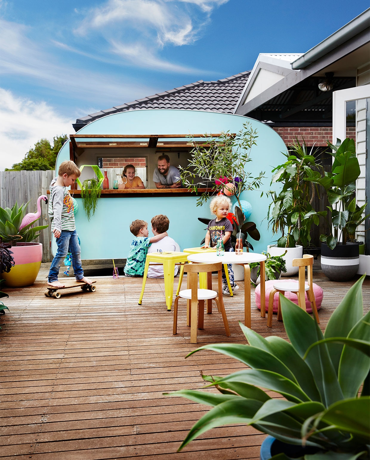 De achtertuin heeft een groot houten dek, waar een oude caravan dienst doet als barretje. Houten tafel en stoelen HipKids. Krukken Tolix. Overig onbekend. vtwonen binnenkijken special 07-2021 | Styling Julia Green en Noel Coughlan | Fotografie Armelle Habib | Tekst Julia Green | Tekstbewerking Caroline Westdijk