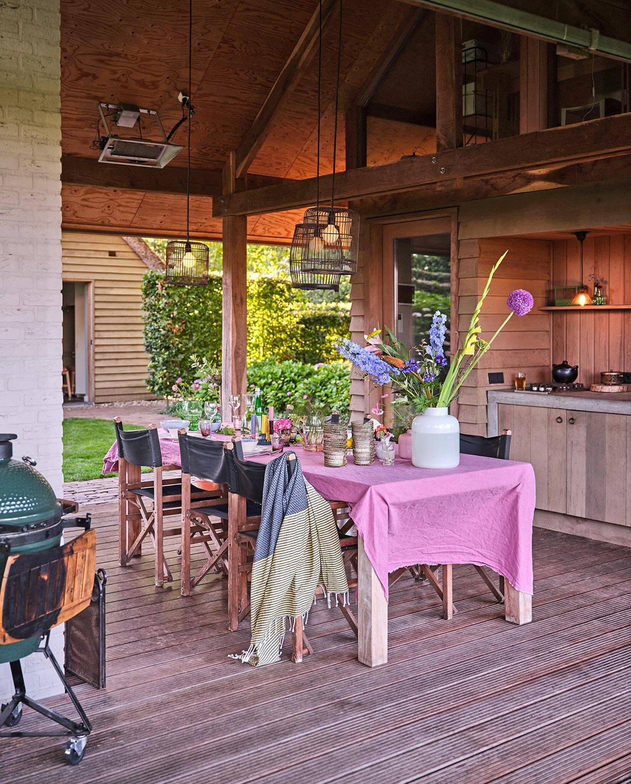Lucas maakte de keuken in het tuinhuis zelf van wrc-delen, rode ceder. De lampen zijn vogelkooien die Carolien zwart heeft gespoten. Het roze tafellaken is een onafgewerkte linnen lap van de markt. Barbecue Green Egg. Hammamdoek Sissy-Boy Homeland. Regisseursstoelen Vervoort Meubelen. De vazen komen overal en nergens vandaan. vtwonen tuin special 3 2021 | styling Carolien Schrievers | fotografie\nRené van der Hulst |