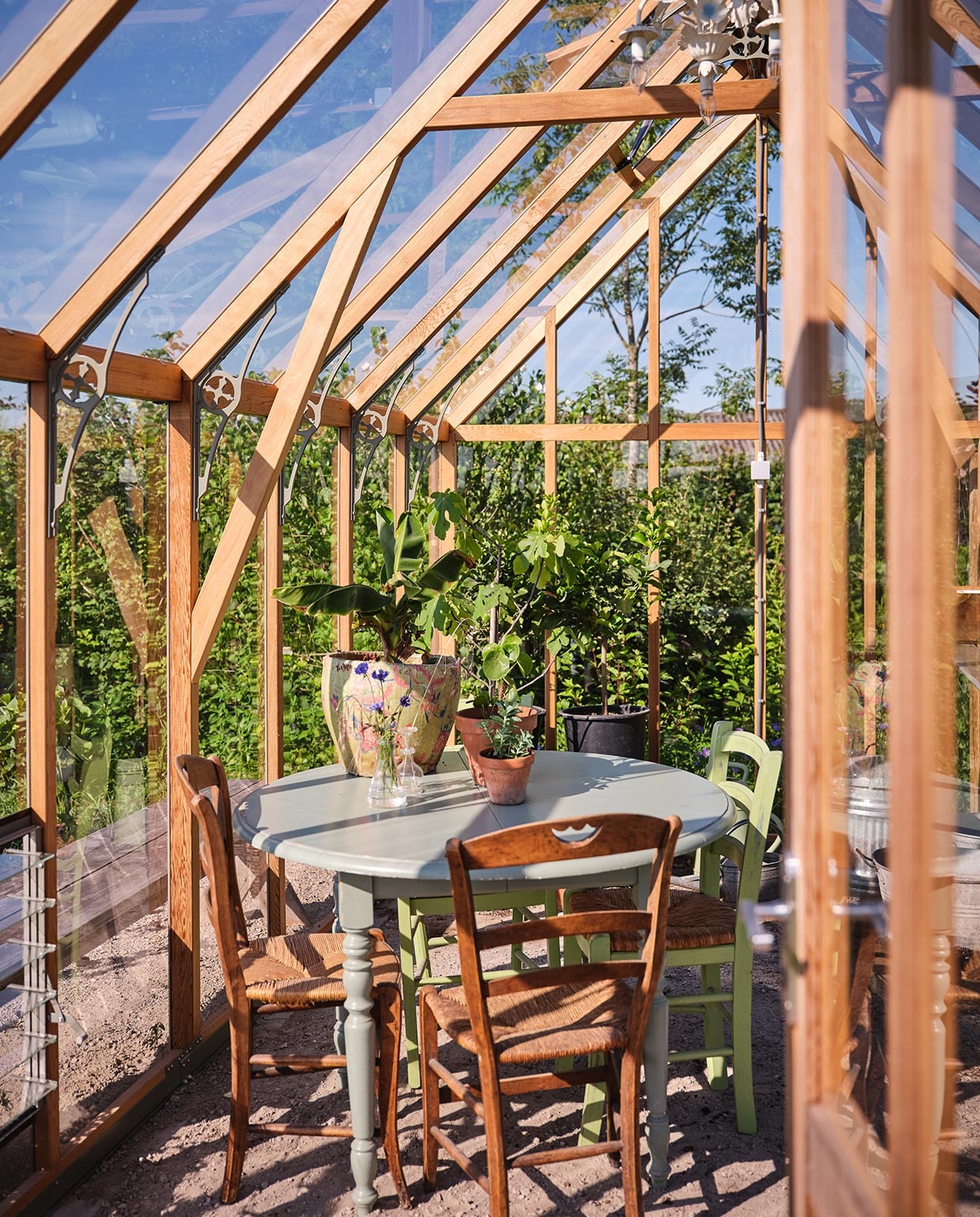 De kas is van Alton en kwam in een bouwpakket via de Tuinkassenwinkel. Erin: een antieke tafel uit Frankrijk, geverfd in een zachtgroene kleur. De antieke stoelen eromheen komen ook uit Frankrijk. vtwonen tuin special 3 2021 | styling Carolien Schrievers | fotografie\nRené van der Hulst |