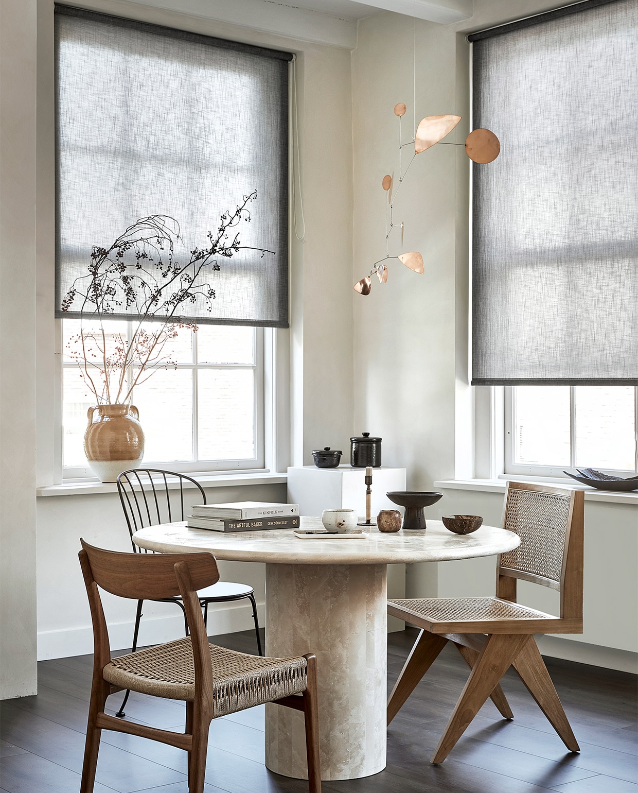 Lichtdoorlatend rolgordijn, op maat gemaakt, in kleur Bruin structuur (18016). M.m.v. karwei.nl (vtwonen EVC vloer kleur Rye), pantoufle-design.nl (tafel), misterdesign.nl (houten stoel CH23 van Carl Hansen, links), casagitane.com (schaal op voet), extravert.nl (stalen stoel Opéra van Fermob), aimetestudio.com (houten stoel Pierre, rechts), zarahome.com (vazen), zenza.nl (alabaster waxinelichthouder), thefinestore.com (kandelaar van Menu), lpln.de (mobile van Lappalainen), bauwerkcolour.com (muurverf in kleur Mykonos). Overig privébezit. vtwonen 09-2021 | productie Tanja Saarberg | styling kim van Rossenberg | fotografie  Peggy Janssen