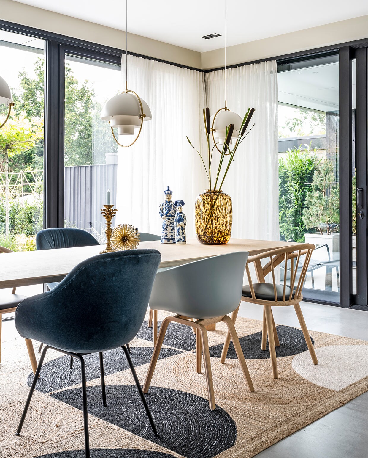 Hanglampen Multi-Lite Gubi, tafel Arp Design, vloerkleed Élitis, donkerblauwe en lichtblauwe stoelen Hay, houten stoelen zwarte zitting Bolia, gouden stekelitem Loods 5, kandelaar palmboom Anna+Nina, beelden Asian Mix Interior, vaas Artic Cheetah Vase the World, linnen gordijnen Interstil. vtwonen 03-2021 | productie CocoFeatures | styling Wendy Verhaegh | fotografie Stan Koolen