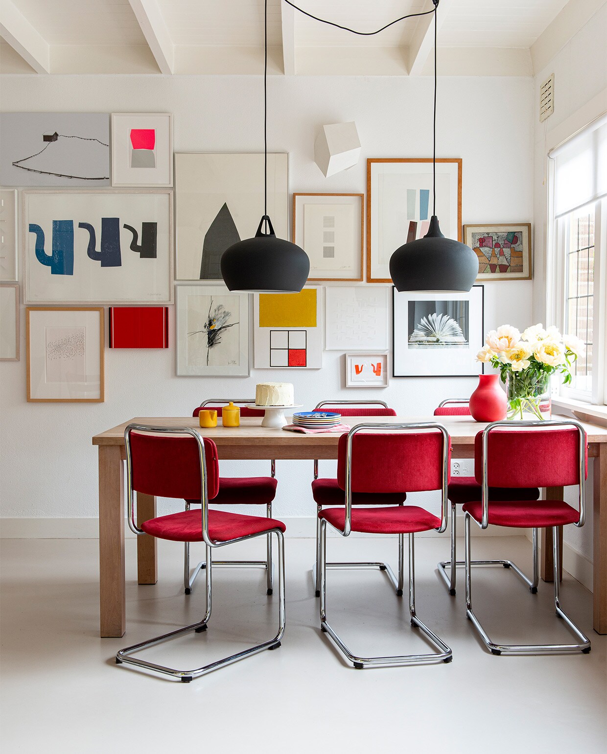 Kunst van onder anderen Albrecht Schnider, Fons Brasser, Alexander Schleber, Jaap Stellaart, Klaas Gubbels, Károly Keserü, Ko Oosterkerk, Reinhard Vrba (Nora’s vader), Hiroshi Harada, Anne Marie Lecluyse en Klaus Staudt. Op tafel vintage melk-en-suikerset, borden Dibbern, vaas Menu, taartplateau Dille &amp; Kamille. Lampen Belly 38 van Nordlux, stoelen Gispen, op maat gemaakte eettafel Jacco Bakker. vtwonen 07-2021 | styling Jeske Weel | fotografie Caroline Coehorst
