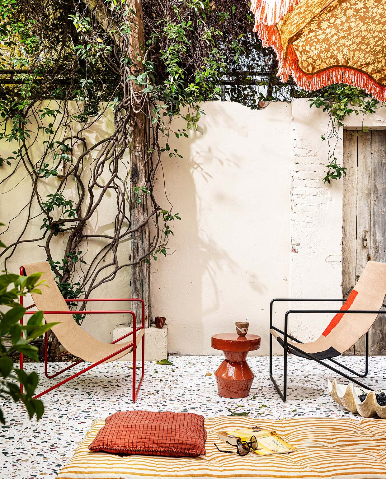 Terrazzo vloer van de buitenplaats styling Capri, 60×60 cm (lxb), voor binnen en buiten, mits onder afdak (tegelbv.com). Stoelen Desert van Ferm Living (vtwonen.nl). Rode bijzettafel (urbannatureculture.com). Gestreept dekmatras 180×70 cm (lxb) en kussenhoes allebei Madam Stoltz (deens.nl). Polystone schelp (nordal.eu). Parasol van HKliving (vtwonen.nl). Kopjes, set van 4 stuks (hkliving.nl). vtwonen 07-2021 | styling Marianne Luning | fotografie Sjoerd Eickmans
