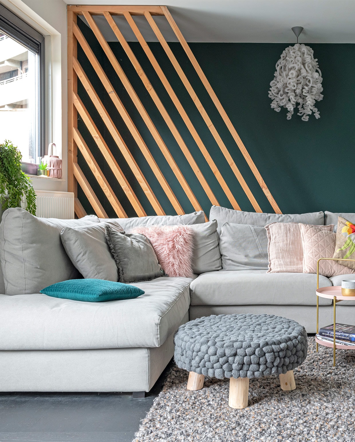 Lattenframe van douglas-hout, gemaakt door bouwbedrijf Klomp. Kleur groen op de wand Quiet Clearing van Histor. Eikenhouten vloer in blokpatroon zwart afgewerkt, vloerkleed, bank LS Napels, kussens, plaid, bijzettafel met draagbeugel, poef Loods 5. Hanglamp, merk onbekend. Bijzettafel met zwart frame Karwei. Kussen met bloem Malagoon. Groen-witte vaas vintage. vtwonen 07-2021 | styling Sharon Roest | fotografie Caroline Martinot