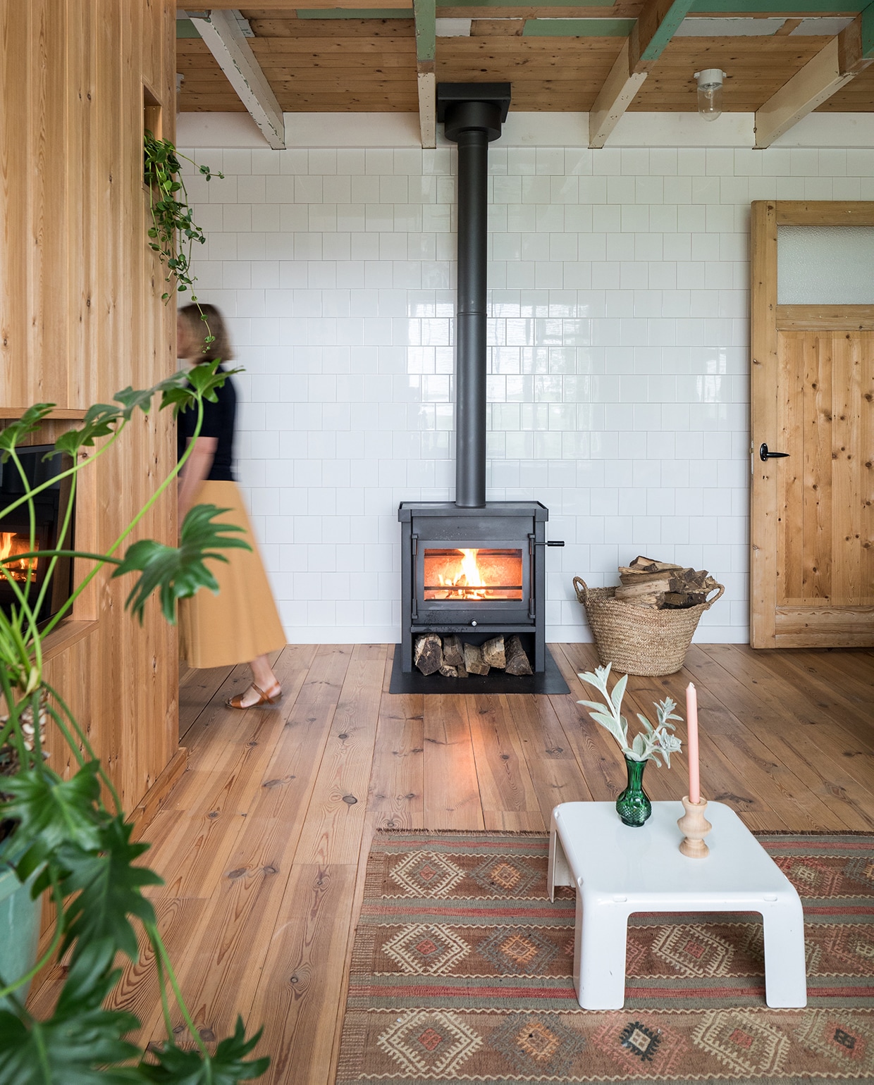Witte hoogglans tegels Praxis, houtkachel Jacobus, houten deur Marktplaats, zelf geloogd. Houtmand, vaas en kandelaar Sip &amp; Clara Pop-up Store. Vintage wit tafeltje B&amp;B Italia, vintage kleed Richard Houpt Noordermarkt Amsterdam.