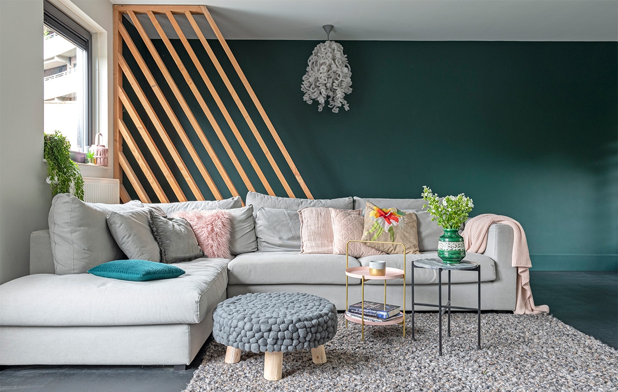 Lattenframe van douglas-hout, gemaakt door bouwbedrijf Klomp. Kleur groen op de wand Quiet Clearing van Histor. Eikenhouten vloer in blokpatroon zwart afgewerkt, vloerkleed, bank LS Napels, kussens, plaid, bijzettafel met draagbeugel, poef Loods 5. Hanglamp, merk onbekend. Bijzettafel met zwart frame Karwei. Kussen met bloem Malagoon. Groen-witte vaas vintage. vtwonen 07-2021 | styling Sharon Roest | fotografie Caroline Martinot