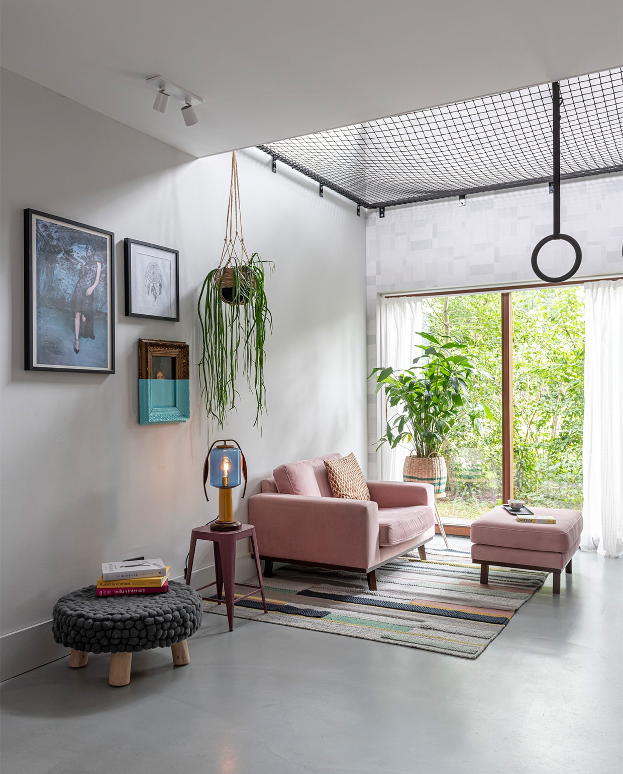 In de woonkeuken met vide hangt een vangnet in een stalen frame, gebouwd door bouwbedrijf Klomp. Net van Van Beelen NTN. Ultratop vloer in betonlook, behang op muur rond raam Norrköping van Engblad &amp; Co. Plafondspot Epic van Maretti. Fauteuil en voetenbank Wehkamp. Vloerkleed Ikea. Poef Loods 5. Aan de wand een ingelijste foto uit boek Sumo van Helmut Newton. Half geverfd schilderij kringloopwinkel. Prent dromenvanger rommelmarkt. Tafellamp Vintkracht Lichtobjecten. Zwarte ringen Bol.com. Manden Tuincentrum Overvecht. Bijzettafels Søstrene Grene. vtwonen 07-2021 | styling Sharon Roest | fotografie Caroline Martinot