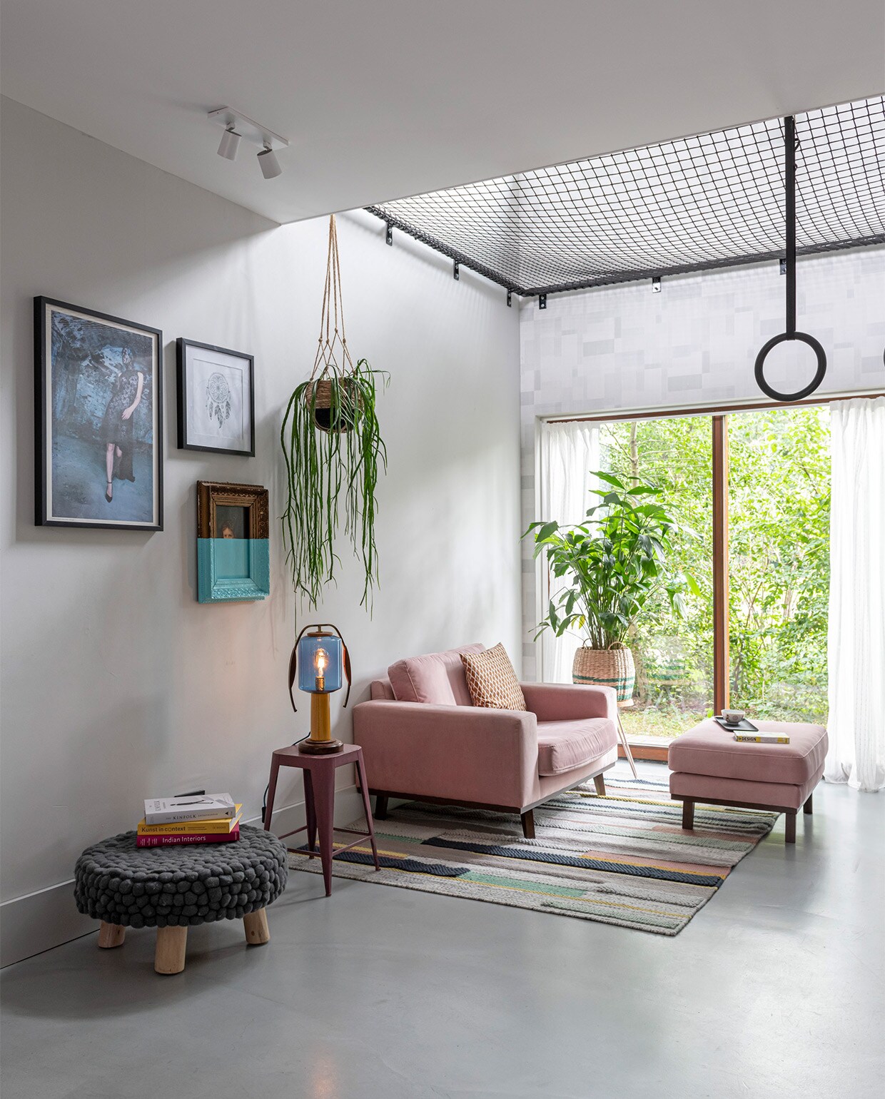 In de woonkeuken met vide hangt een vangnet in een stalen frame, gebouwd door bouwbedrijf Klomp. Net van Van Beelen NTN. Ultratop vloer in betonlook, behang op muur rond raam Norrköping van Engblad &amp; Co. Plafondspot Epic van Maretti. Fauteuil en voetenbank Wehkamp. Vloerkleed Ikea. Poef Loods 5. Aan de wand een ingelijste foto uit boek Sumo van Helmut Newton. Half geverfd schilderij kringloopwinkel. Prent dromenvanger rommelmarkt. Tafellamp Vintkracht Lichtobjecten. Zwarte ringen Bol.com. Manden Tuincentrum Overvecht. Bijzettafels Søstrene Grene. vtwonen 07-2021 | styling Sharon Roest | fotografie Caroline Martinot