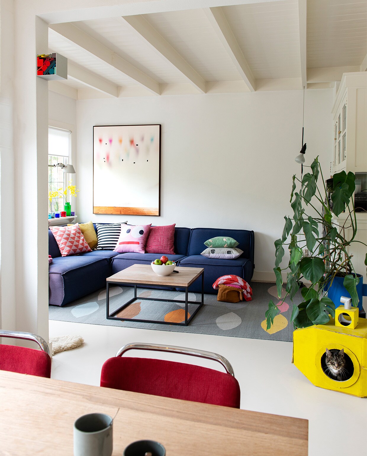 Kubus met kleuren van Sophie Smallhorn. Op de vensterbank: lamp Tolomeo van Artemide, theelichten Iittala. Bank Edge van Fest Amsterdam, kussens van diverse herkomst, fotografisch kunstwerk van Katja Mater via Galerie Heden, salontafel laten maken door smid, schaal Bebouwde Kom van Olav Slingerland, karpet Leaves van CarpetVista, in de hoek lamp Parentesi van Flos, blauwe bloempot Serax, stoelen model 101 van Gispen, op maat gemaakte eettafel Jacco Bakker, mokken De Intuïtiefabriek. vtwonen 07-2021 | styling Jeske Weel | fotografie Caroline Coehorst