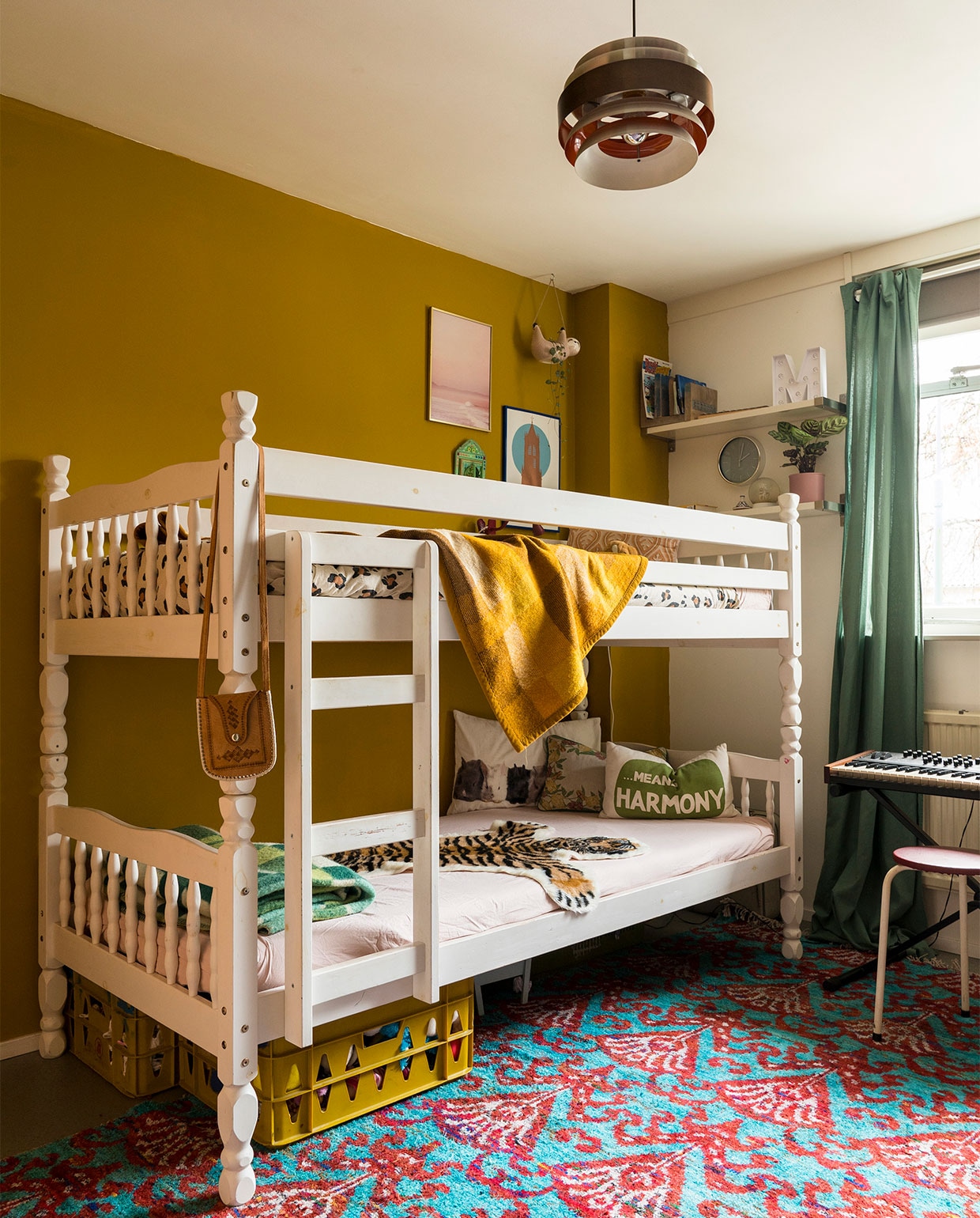 Verfkleur op de wand Komijn van Gamma. Bed via Marktplaats. Beddengoed en luiaard Kwantum. Gele en groene wollen dekens kringloopwinkel. Kussen met geel motief Auping. Roze print IrisDorine. Domtoren We are out of office. Kratten kringloopwinkel. Konijnenkussen Ikea. Kussen met Means Harmony H&amp;M Home. Gebloemd kussen kringloopwinkel. Tijger herkomst onbekend. Spiegeltje uit Marokko. Vloerkleed Marktplaats. Gordijn Kwantum. Wandplankjes Ikea. Letter M Hema. Klok herkomst onbekend. Hanglamp Marktplaats. Krukje kringloopwinkel. Synthesizer privébezit. Tasje herkomst onbekend. vtwonen 07-2021 | fotografie Muk van Lil | tekst Monique Butter