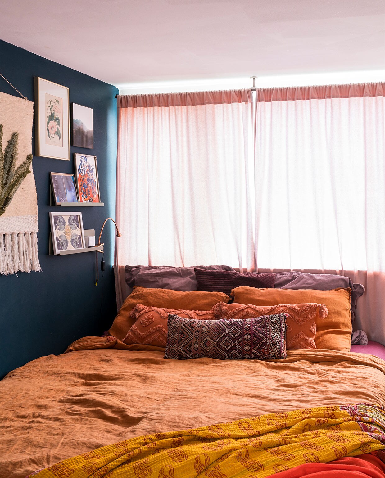 Verfkleur op de wand Hague Blue Farrow &amp; Ball. Plankjes Søstrene Grene. Wandkleed Sissy-Boy. Prent met bloemen kringloopwinkel. Landschap IrisDorine. Foto privébezit. Oranje prent maakster onbekend. Onderste prent Hanneke van de Pol. Klemlampje Ikea. Gordijnen H&amp;M Home. Terracottakleurig beddengoed La Redoute. Terracottakleurige kussens met motief Hema. Geborduurd kussen uit Marokko. Grote kussens Dille &amp; Kamille. Geribbeld kussen Hema. Kanthakleed uit India. Rode sjaal Scotch &amp; Soda. vtwonen 07-2021 | fotografie Muk van Lil